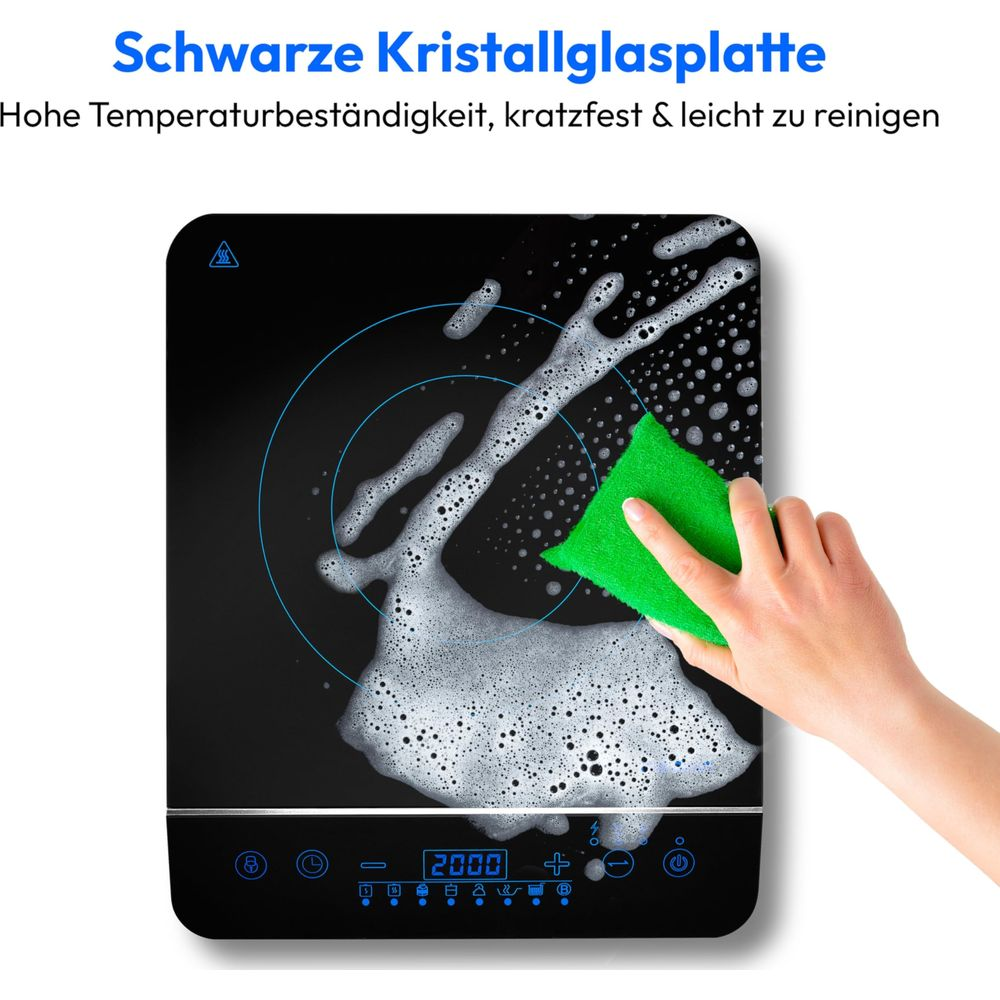 Ręka czyści czarną płytę kuchenną pianą i zieloną gąbką.