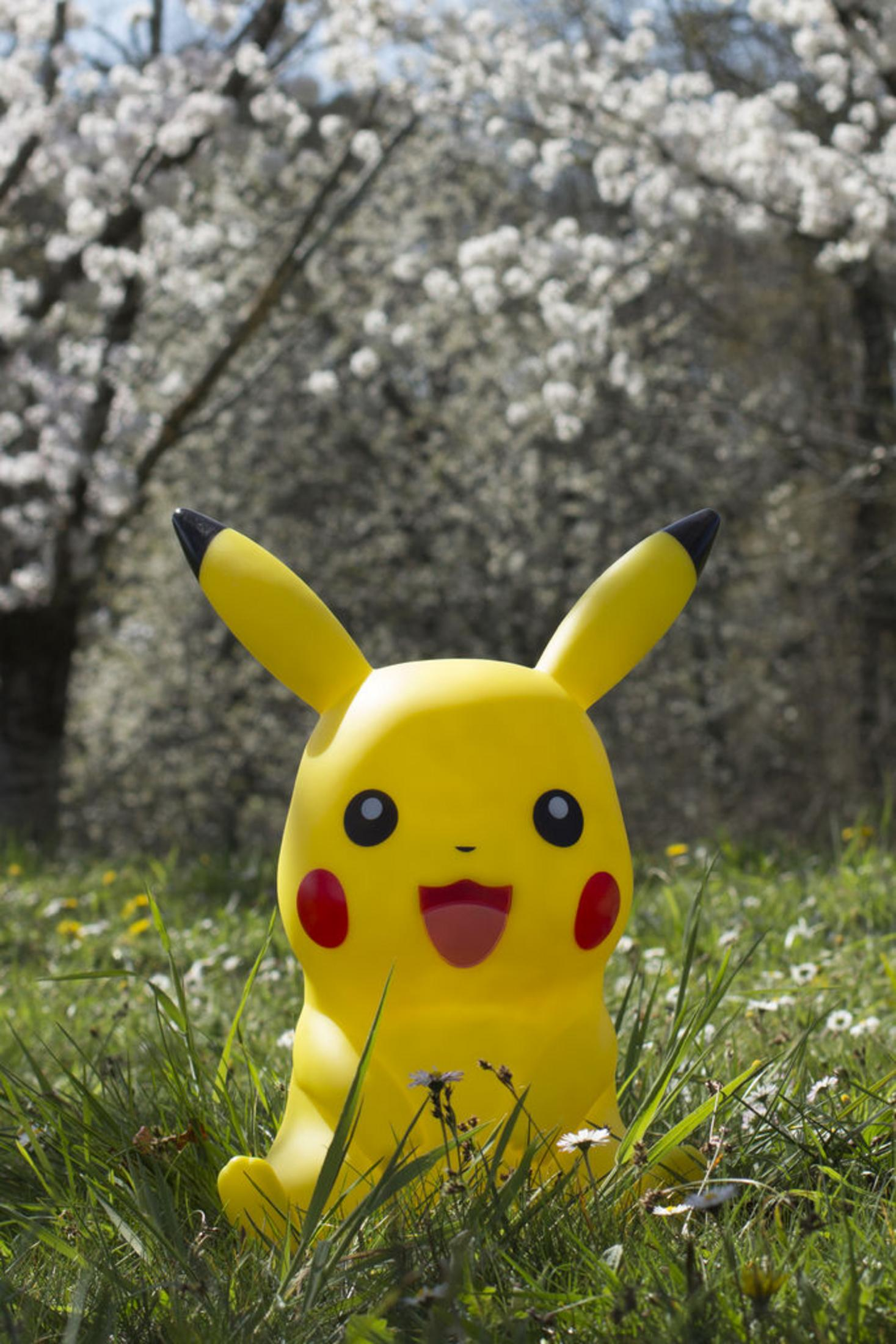 Una figura gialla di Pikachu siede in erba verde con piccoli fiori bianchi.
