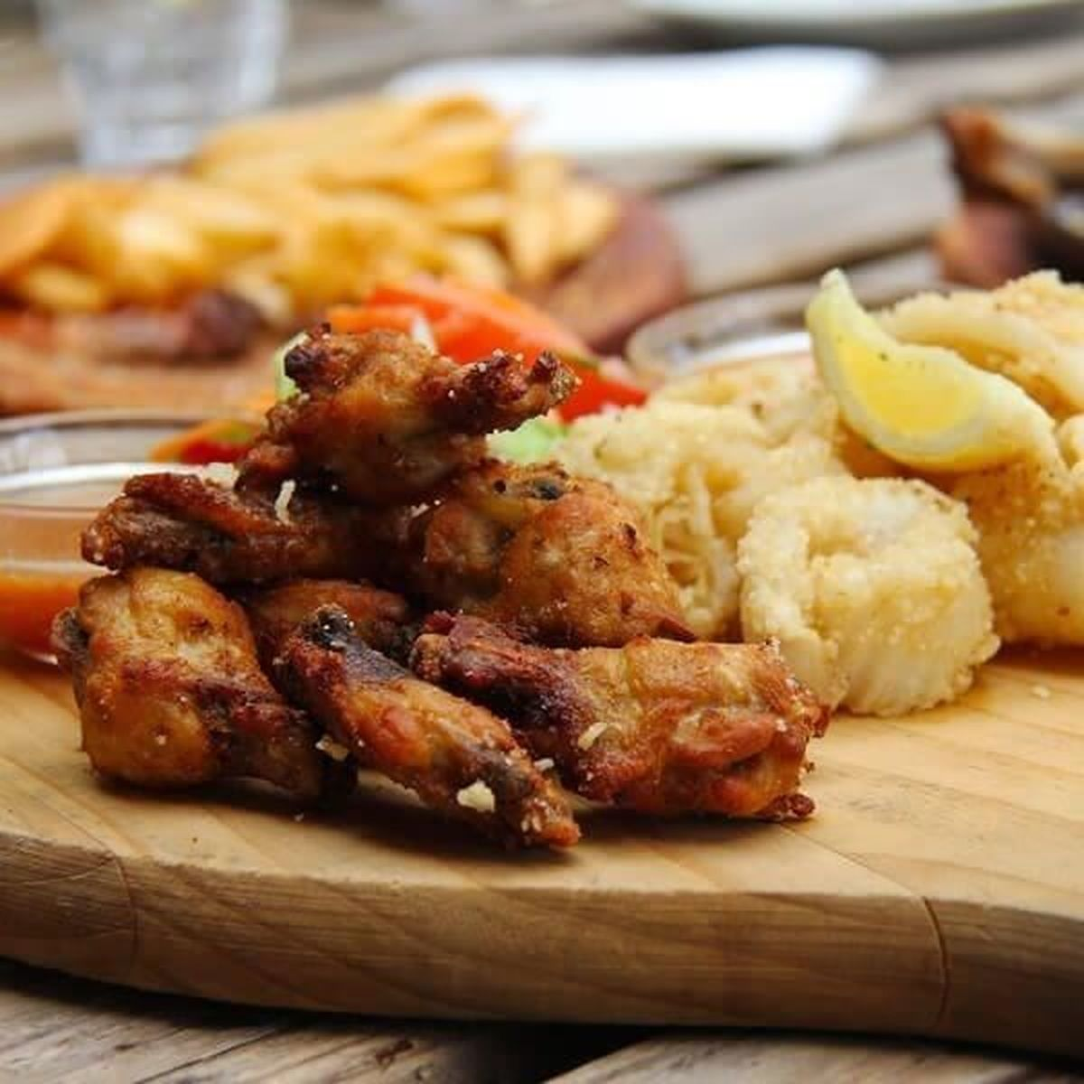 Chrupiące skrzydełka kurczaka z frytkami i ćwiartką cytryny na desce.