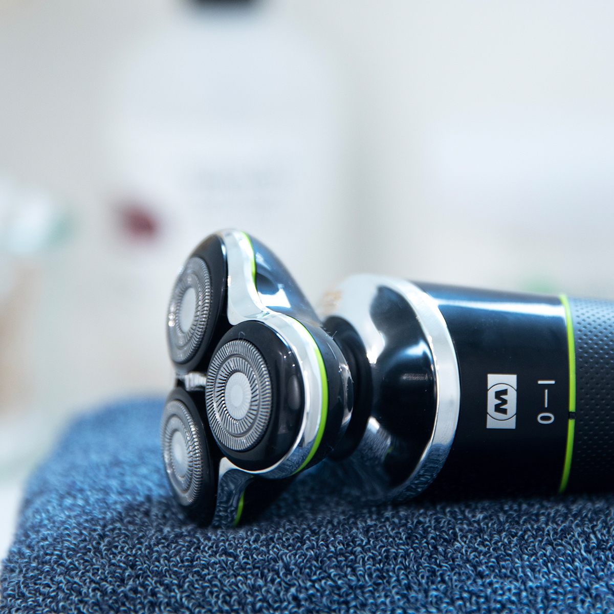 Czarna golarka elektryczna z trzema obrotowymi głowicami leży na niebieskim ręczniku.