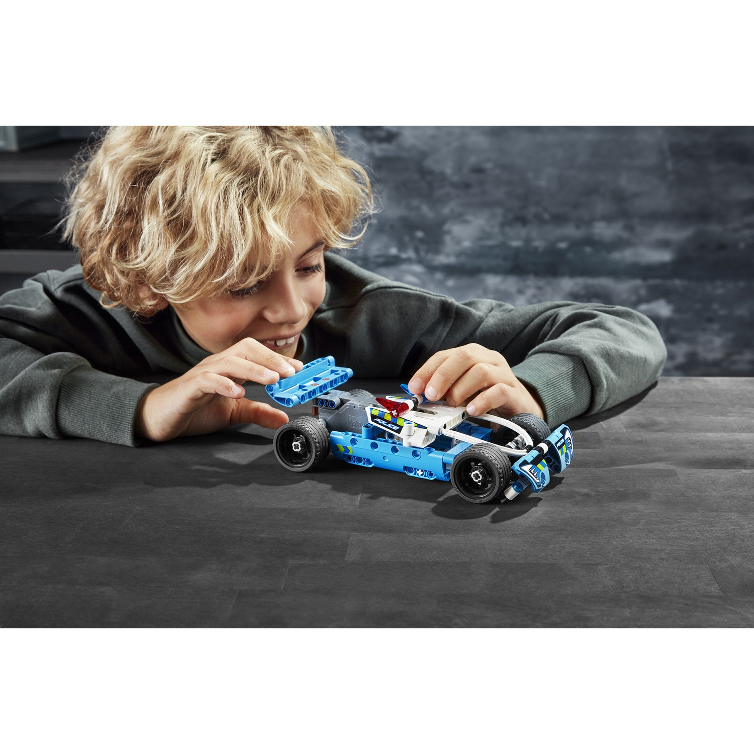 Un ragazzo costruisce un'auto della polizia LEGO blu su un tavolo.