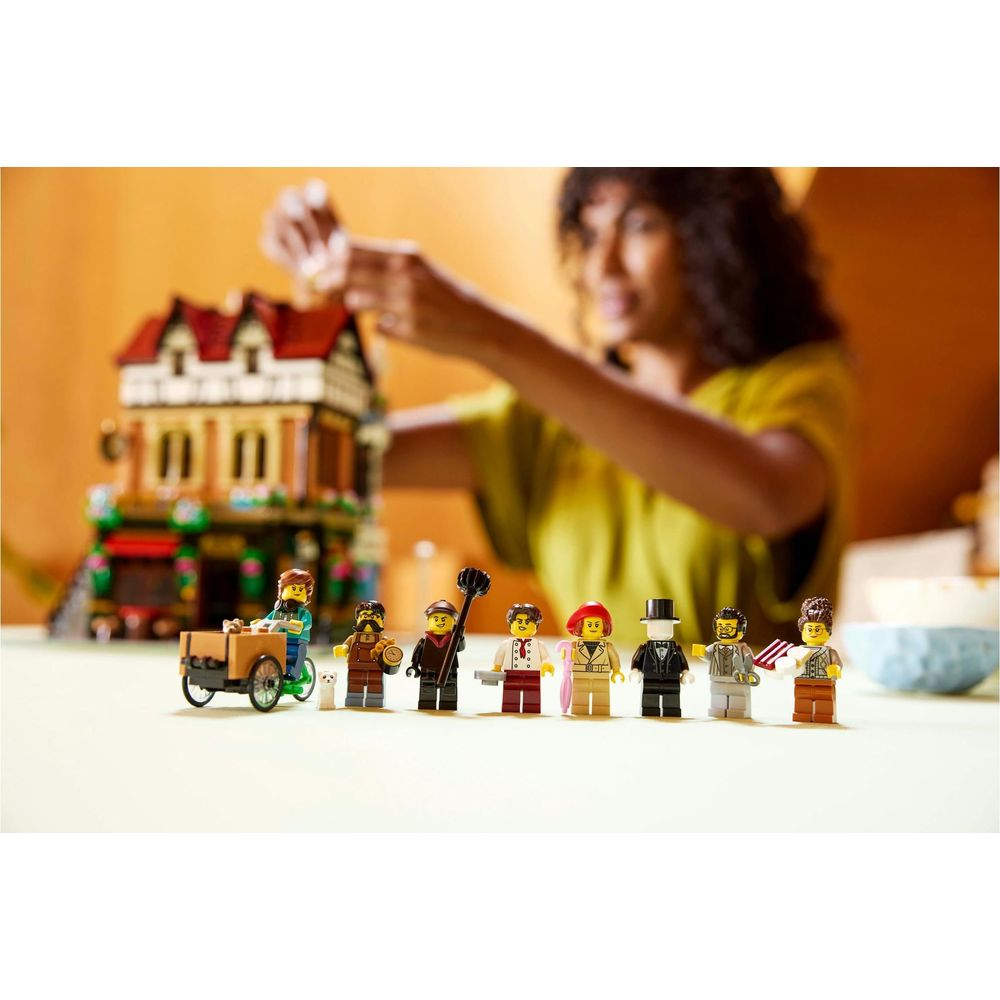 Figurki Lego przed domem Lego, kobieta buduje w tle.