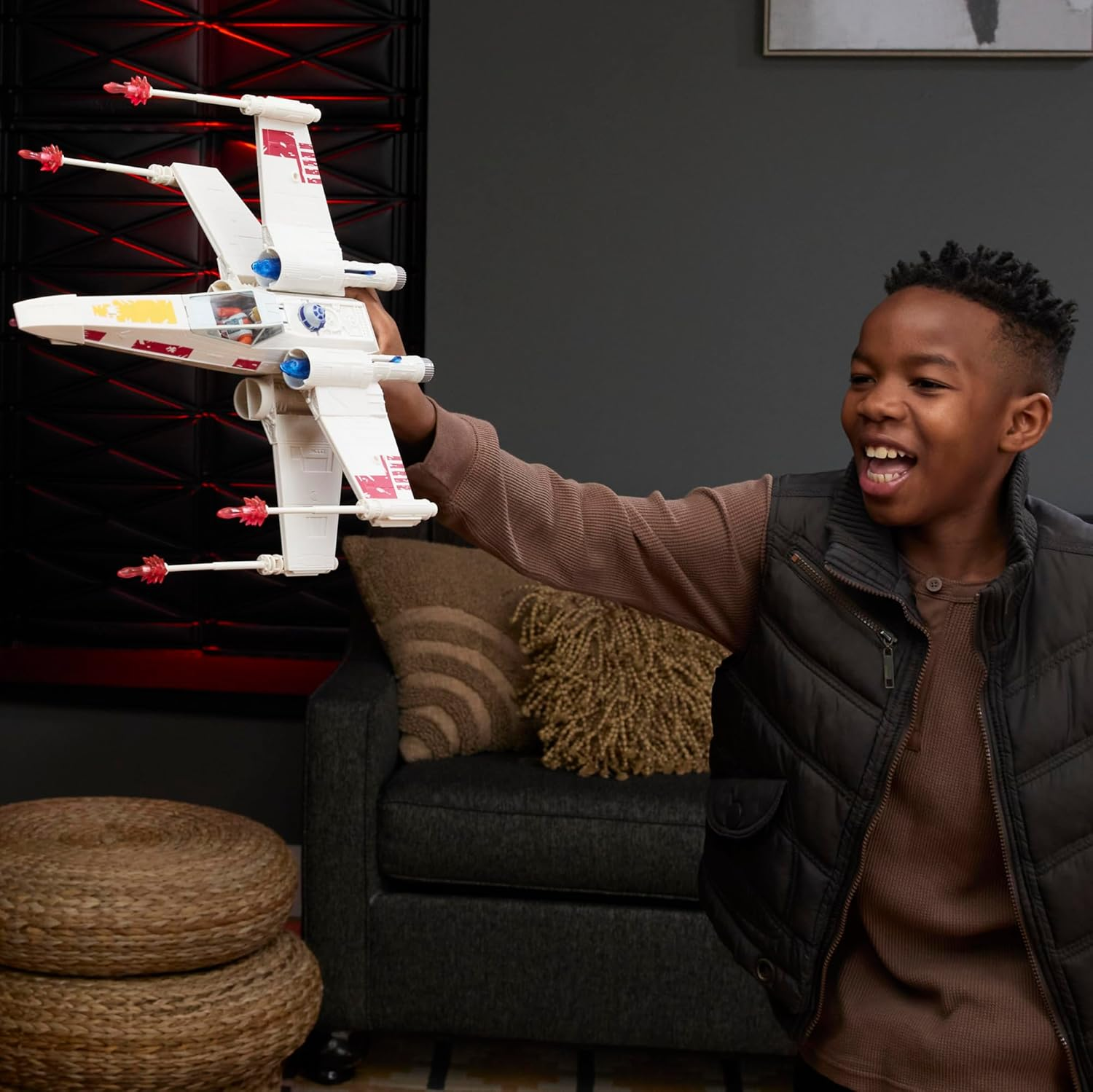 Un niño sostiene un juguete X-Wing blanco delante de él. Fondo oscuro.