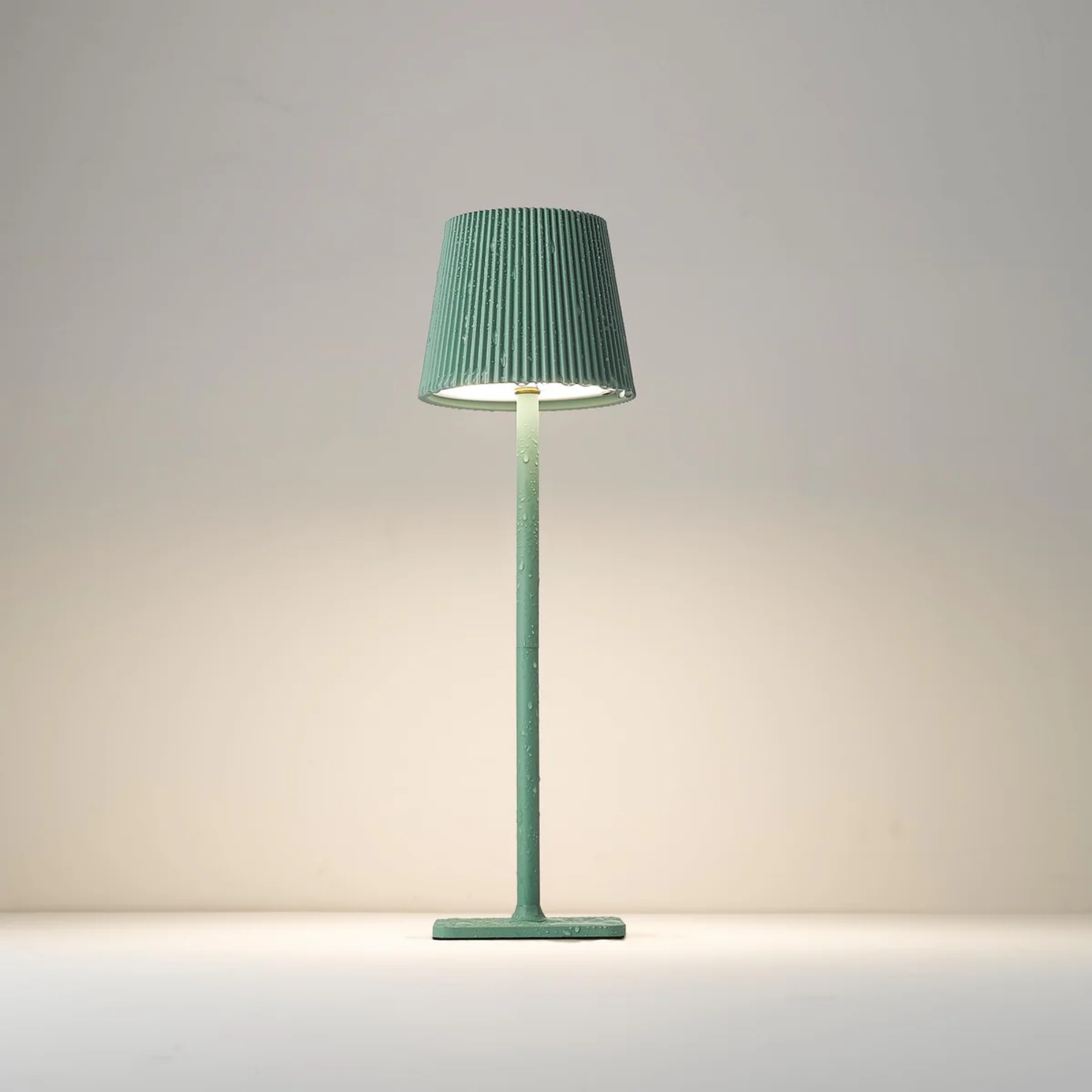 Eine grüne Lampe mit geripptem Schirm, die Wasserperlen aufweist.