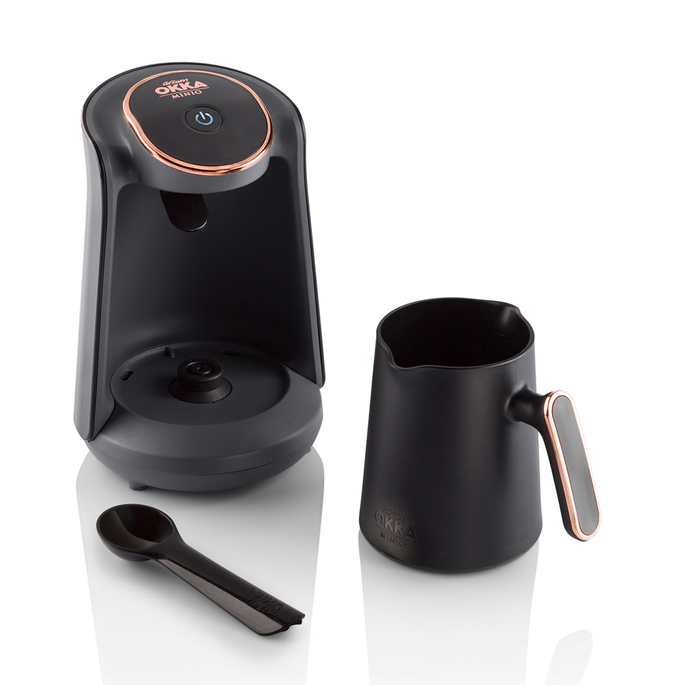 Schwarze Kaffeemaschine mit Kanne und Löffel, Rosegold-Akzenten.