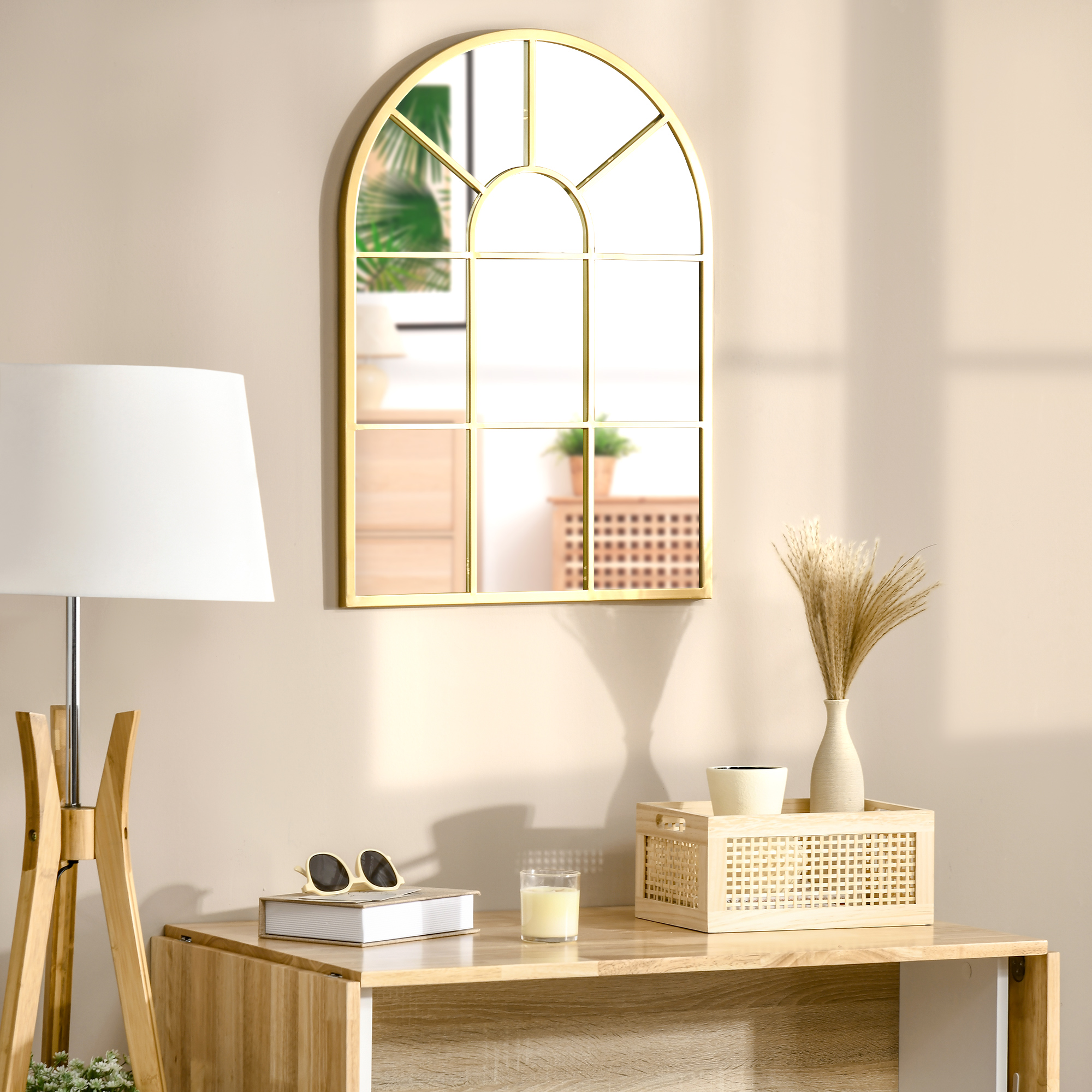 Un espejo arqueado con marco dorado cuelga sobre mesa de madera con lámpara, libro y gafas.