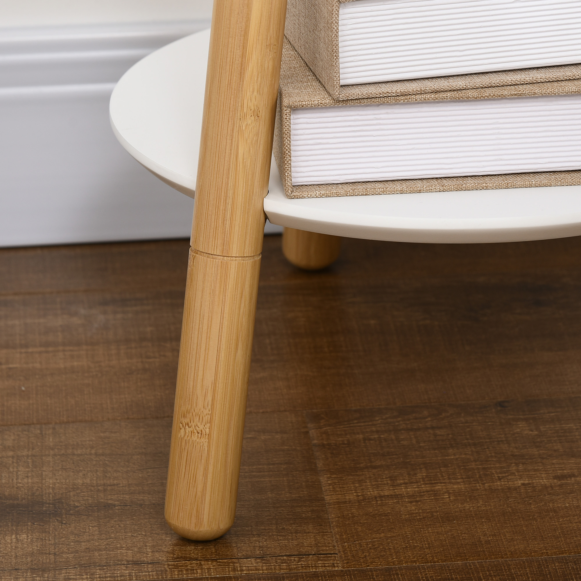 Una pata de bambú sostiene una mesa blanca con dos libros encima. Suelo de madera.