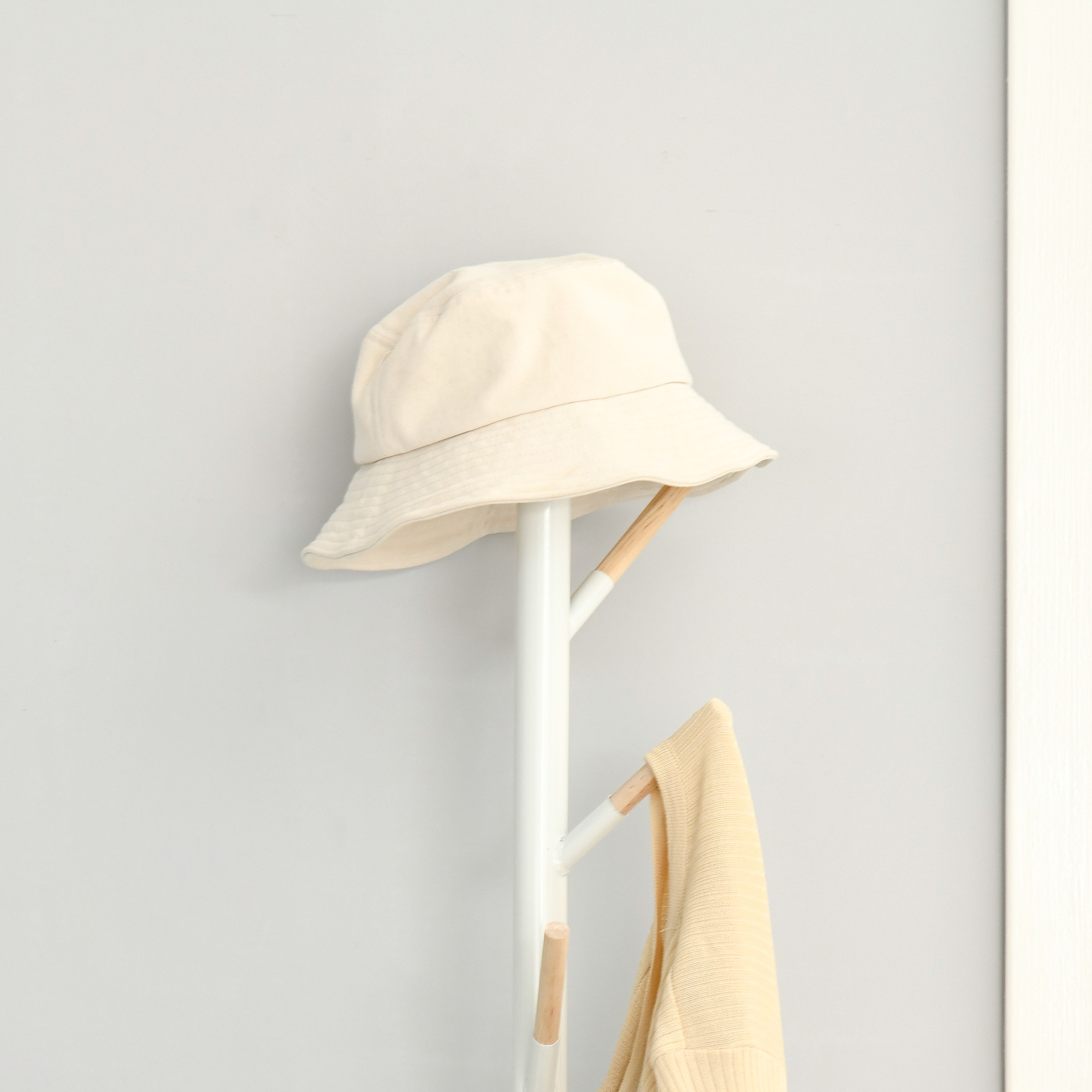 Un sombrero de pescador beige y un suéter amarillo cuelgan de un perchero blanco.