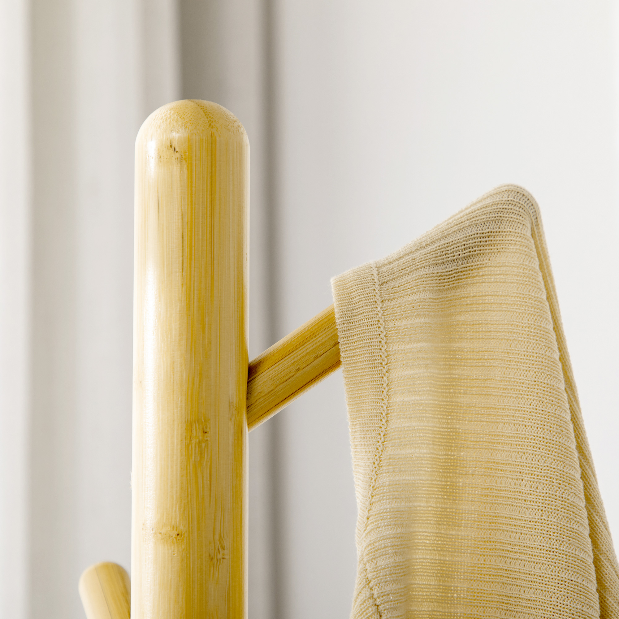 Un suéter beige cuelga de un soporte de madera con un patrón de punto fino.