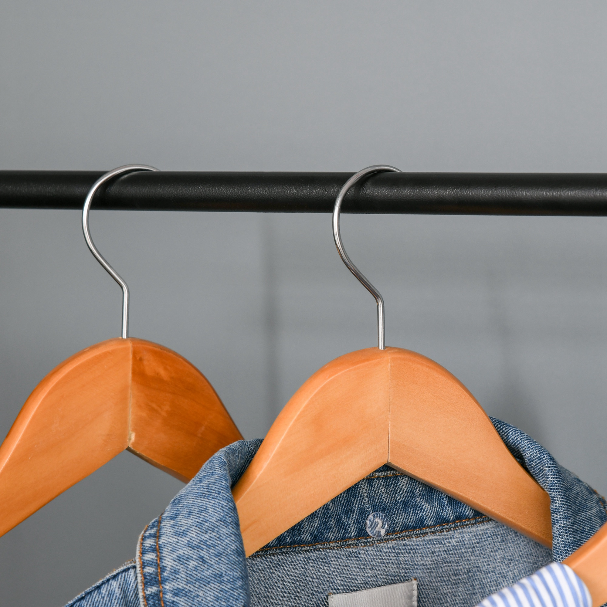 Dos perchas de madera con ropa en una barra contra un fondo gris.