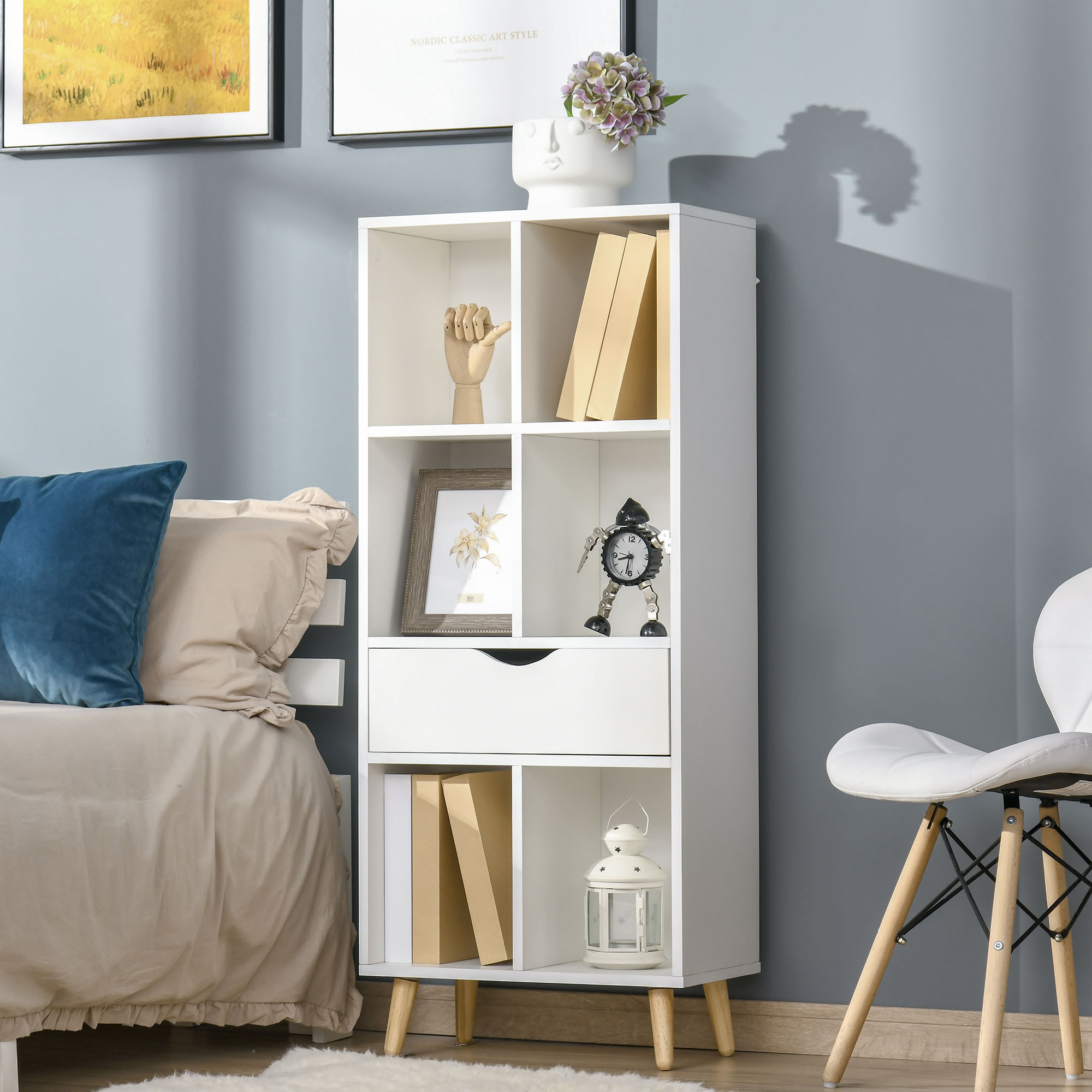 Una estantería blanca con libros, una foto y un reloj junto a una cama.