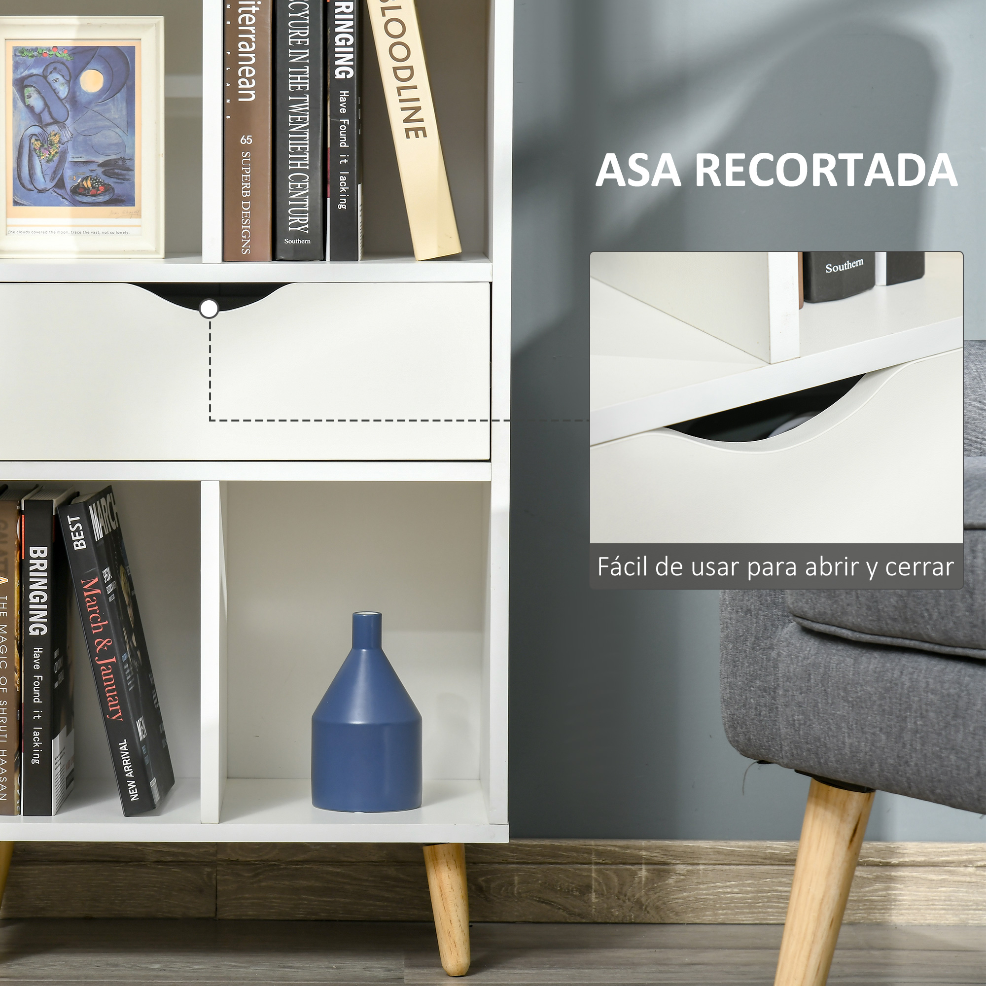 Estante blanco con libros, cuadro y jarrón azul. Un sillón gris al lado.