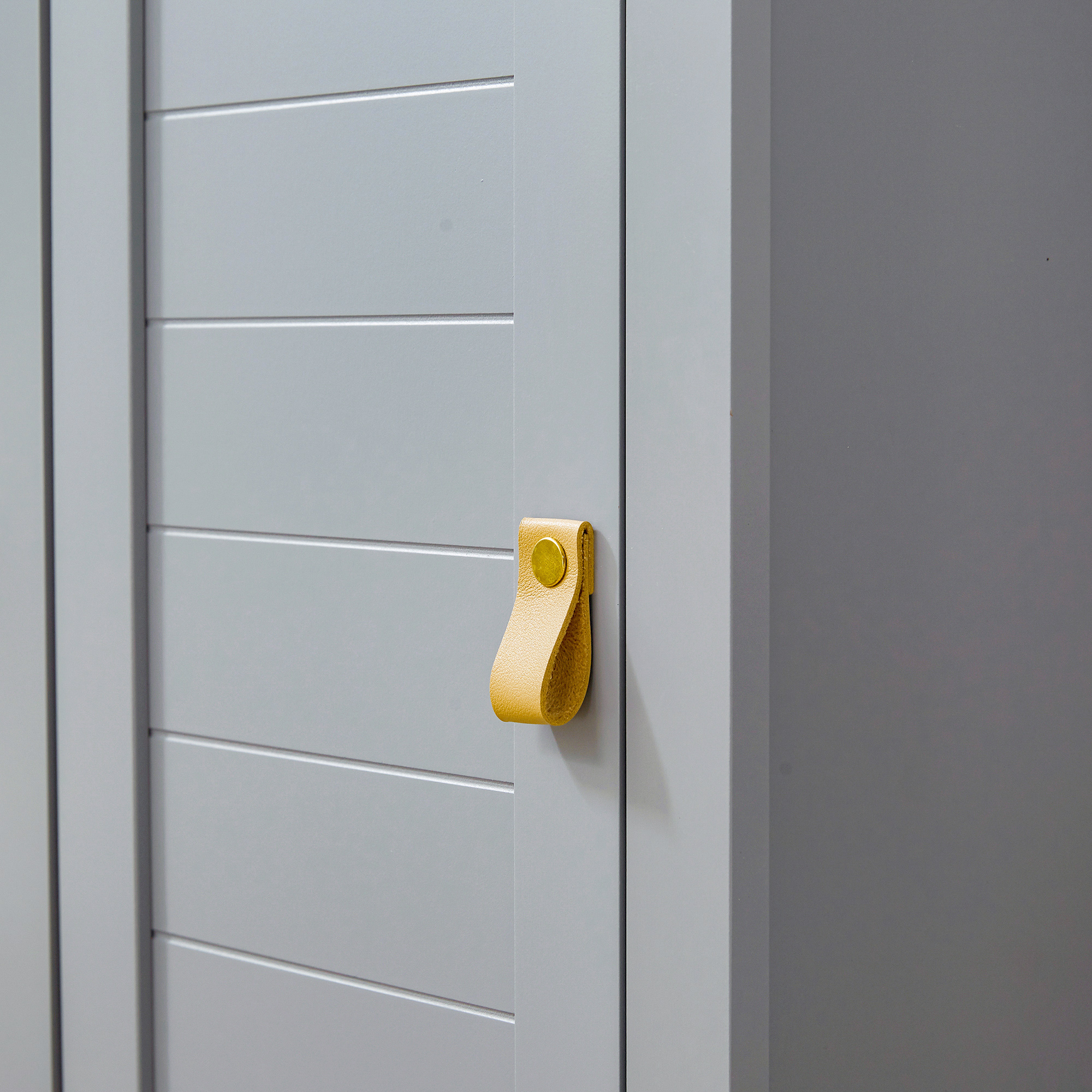Puerta de armario gris con ranuras horizontales y un tirador de cuero amarillo.