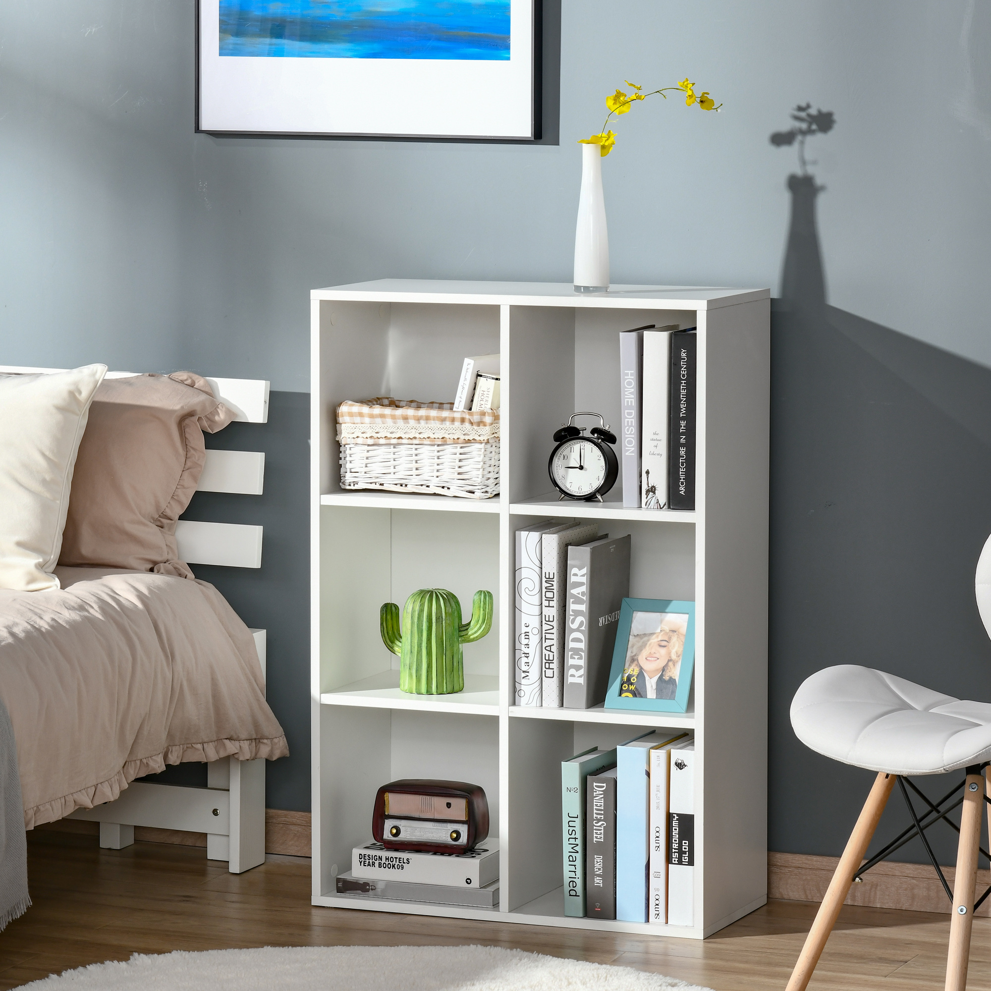 Un estante blanco con libros, un jarrón, un cactus y una radio.