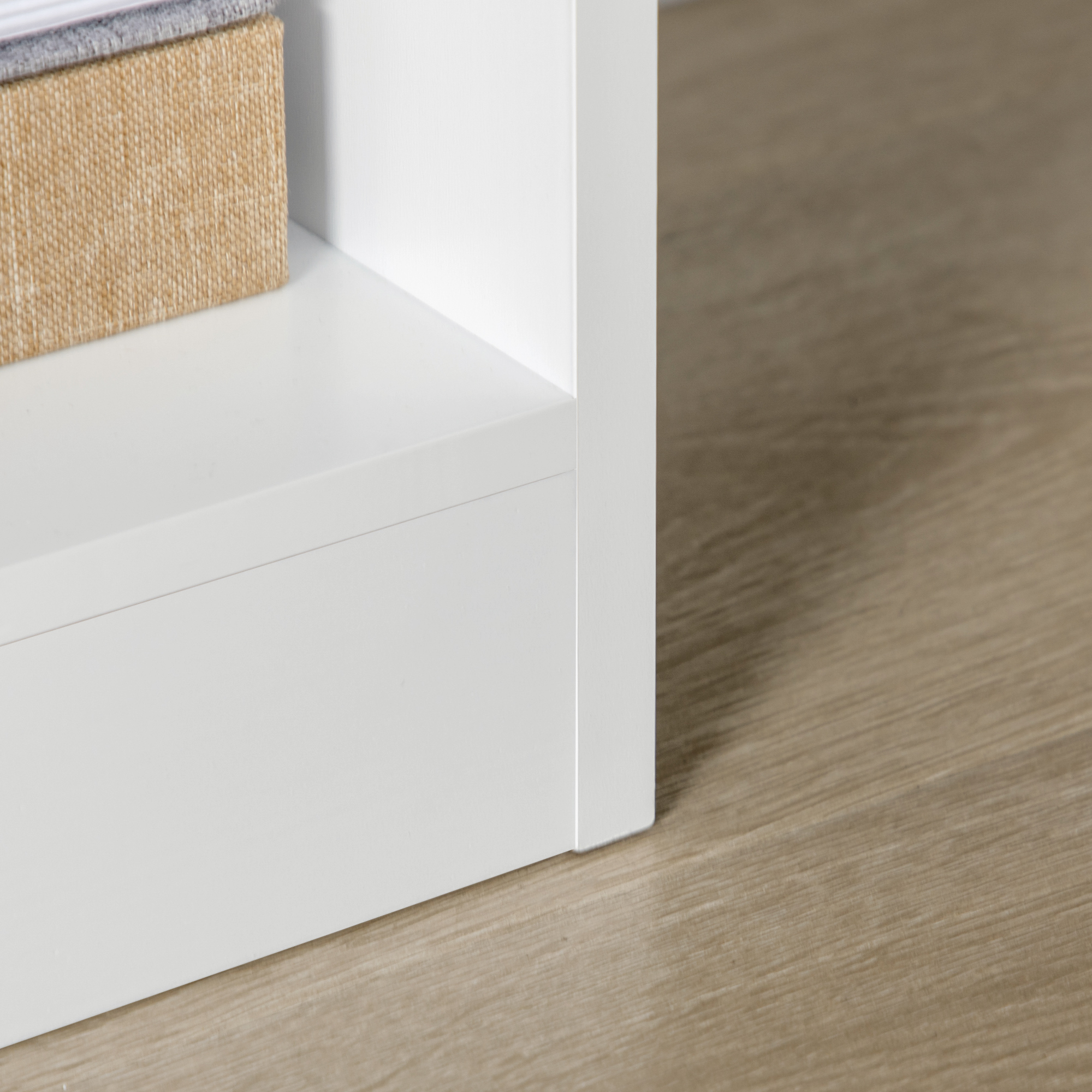 Una caja tejida beige en un estante blanco junto a un piso de madera.