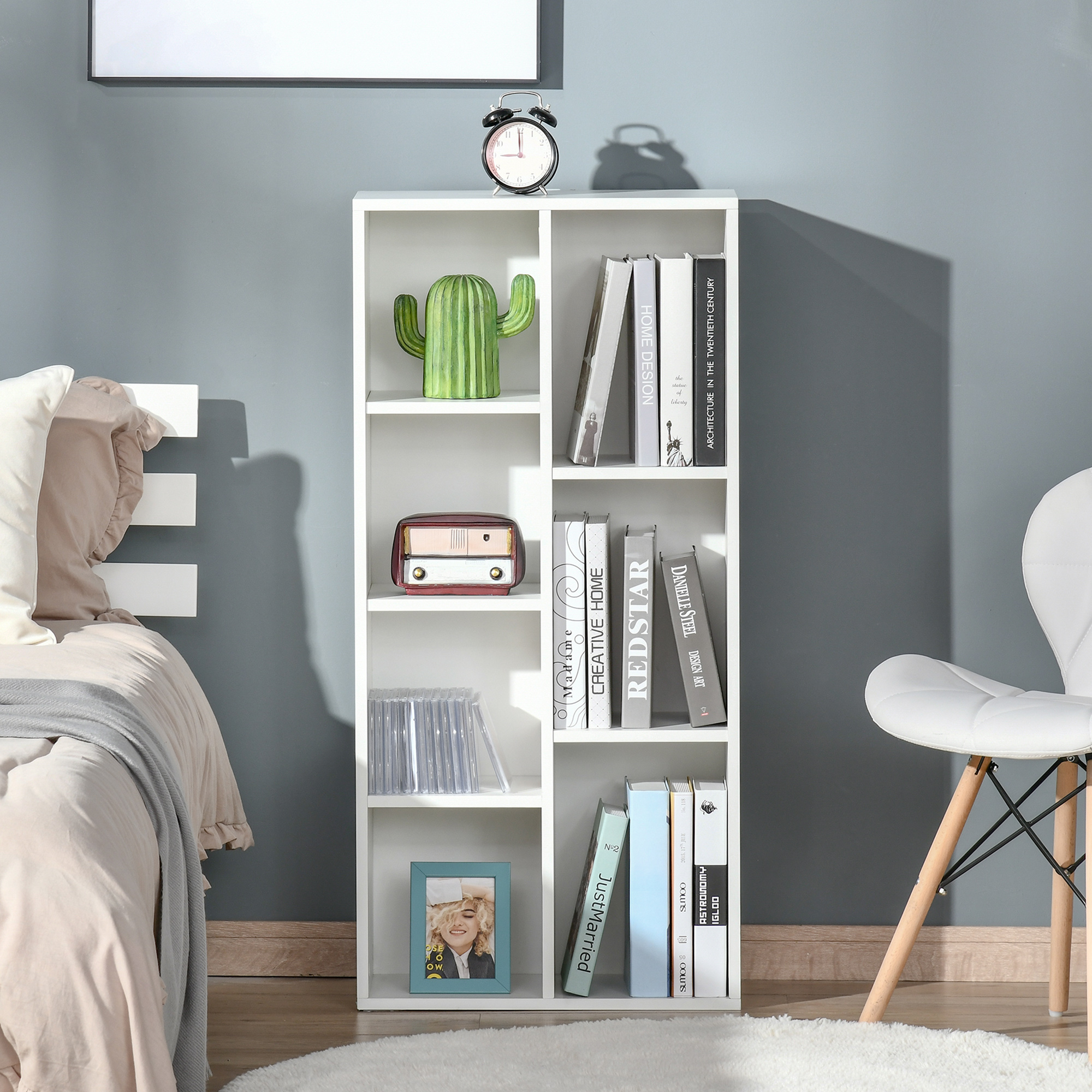 Una estantería blanca con libros, un cactus, una radio y un marco de fotos en un dormitorio.