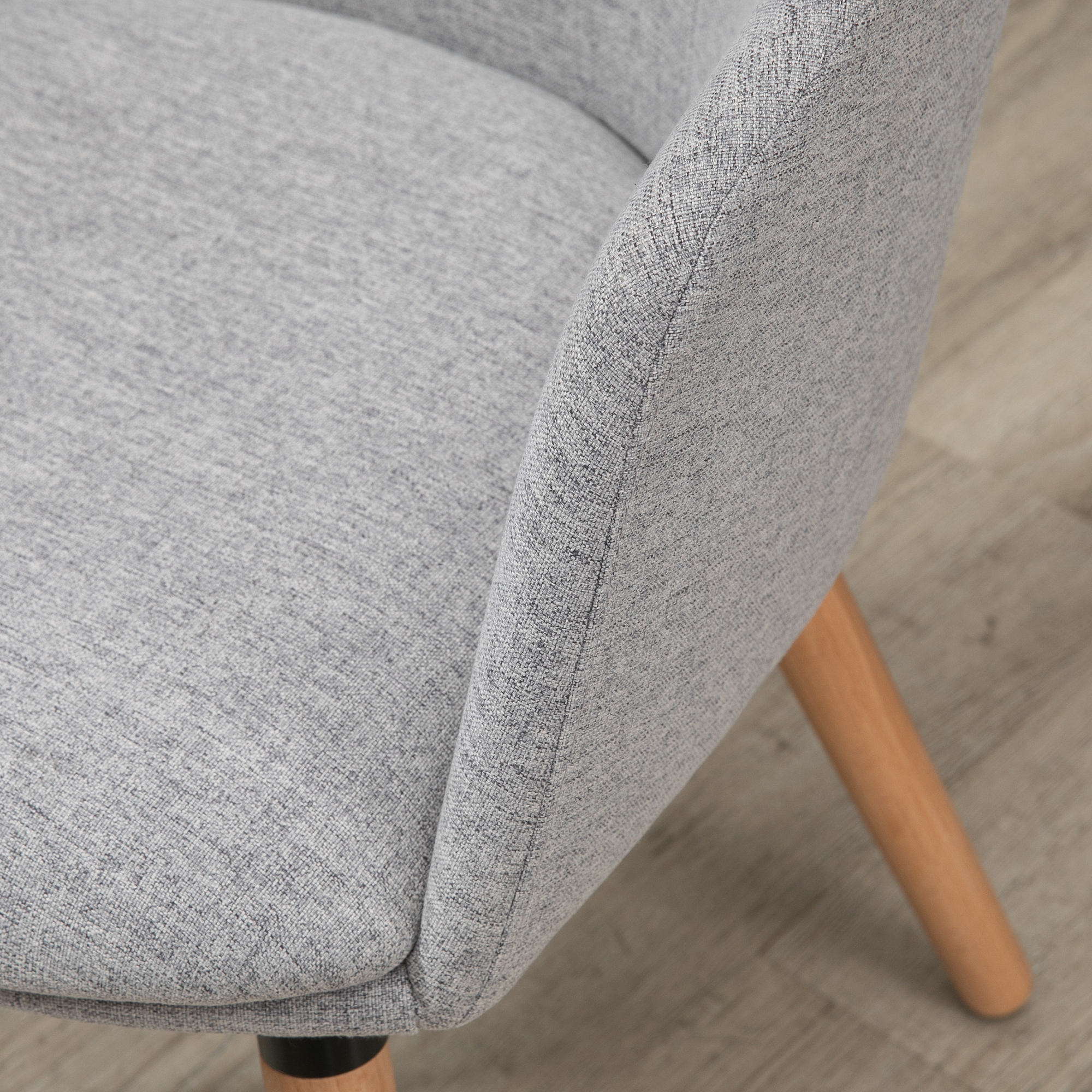Silla de tela gris con pata de madera sobre suelo de madera.