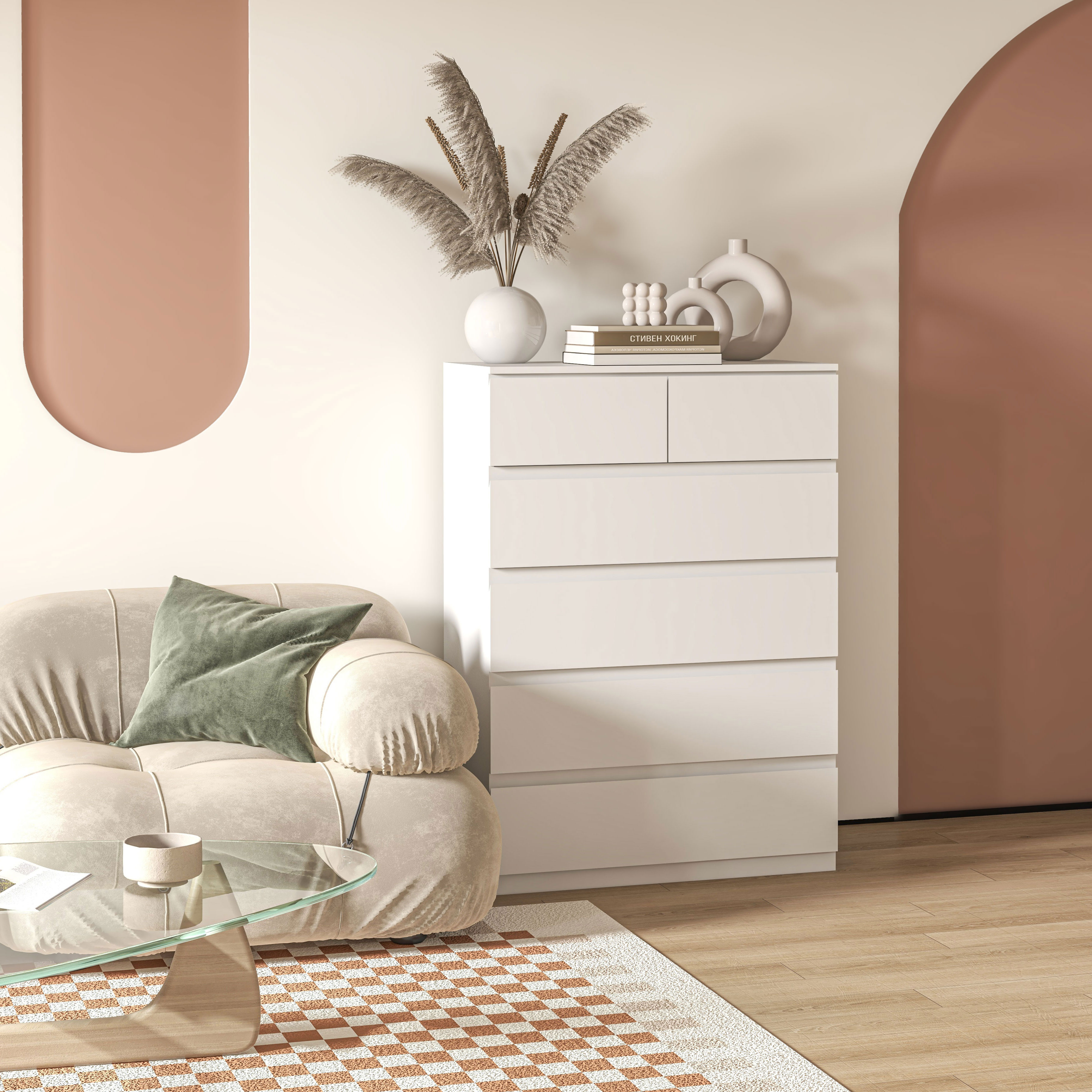 Un sofá beige con cojín, mesa de cristal y cómoda blanca con libros.