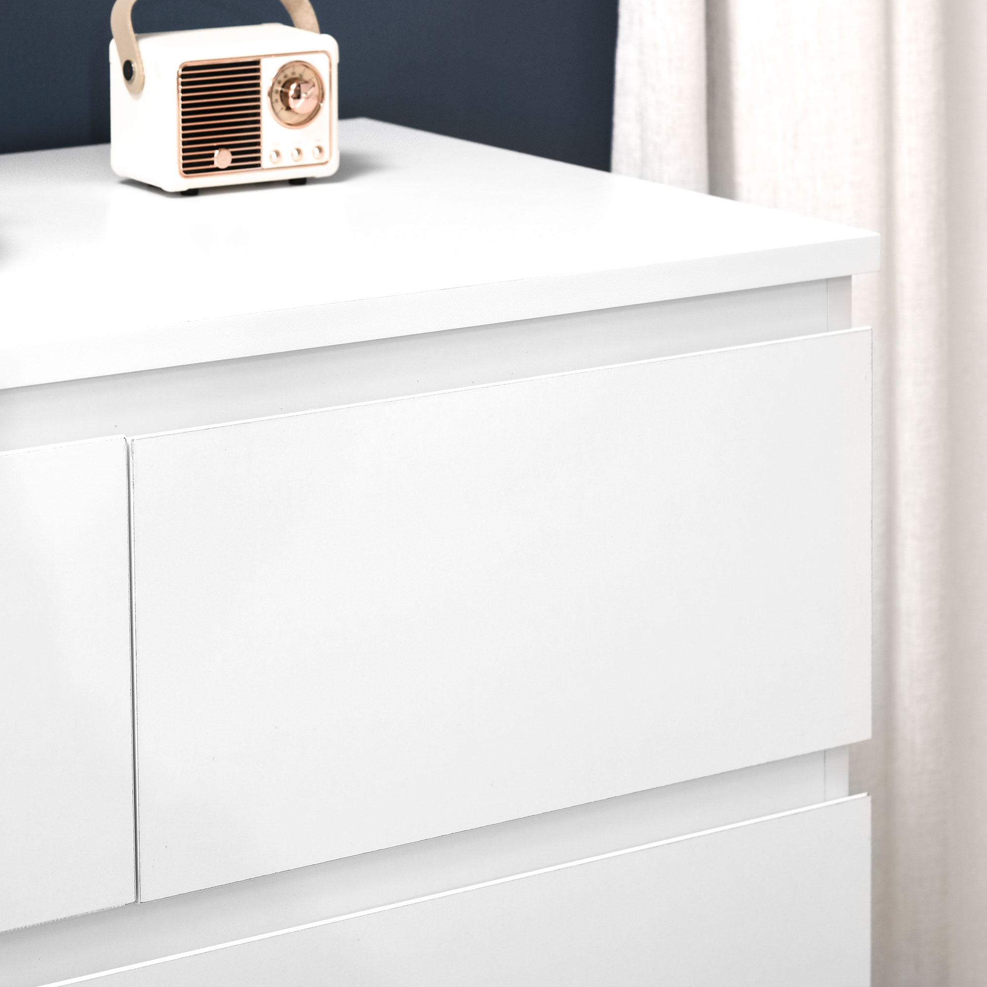 Una radio blanca con detalles en cobre sobre una cómoda blanca.