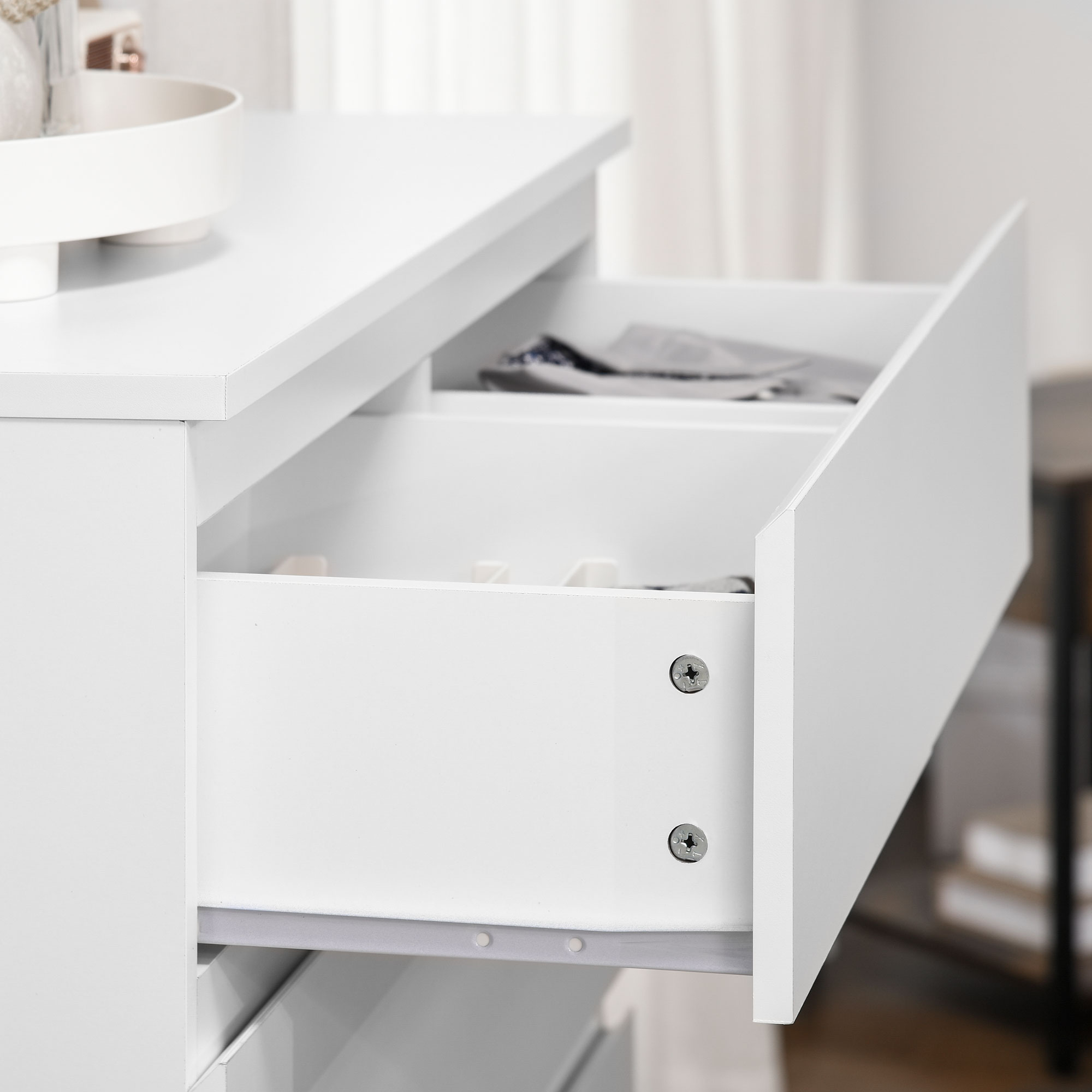 Cómoda blanca con un cajón abierto que contiene ropa.