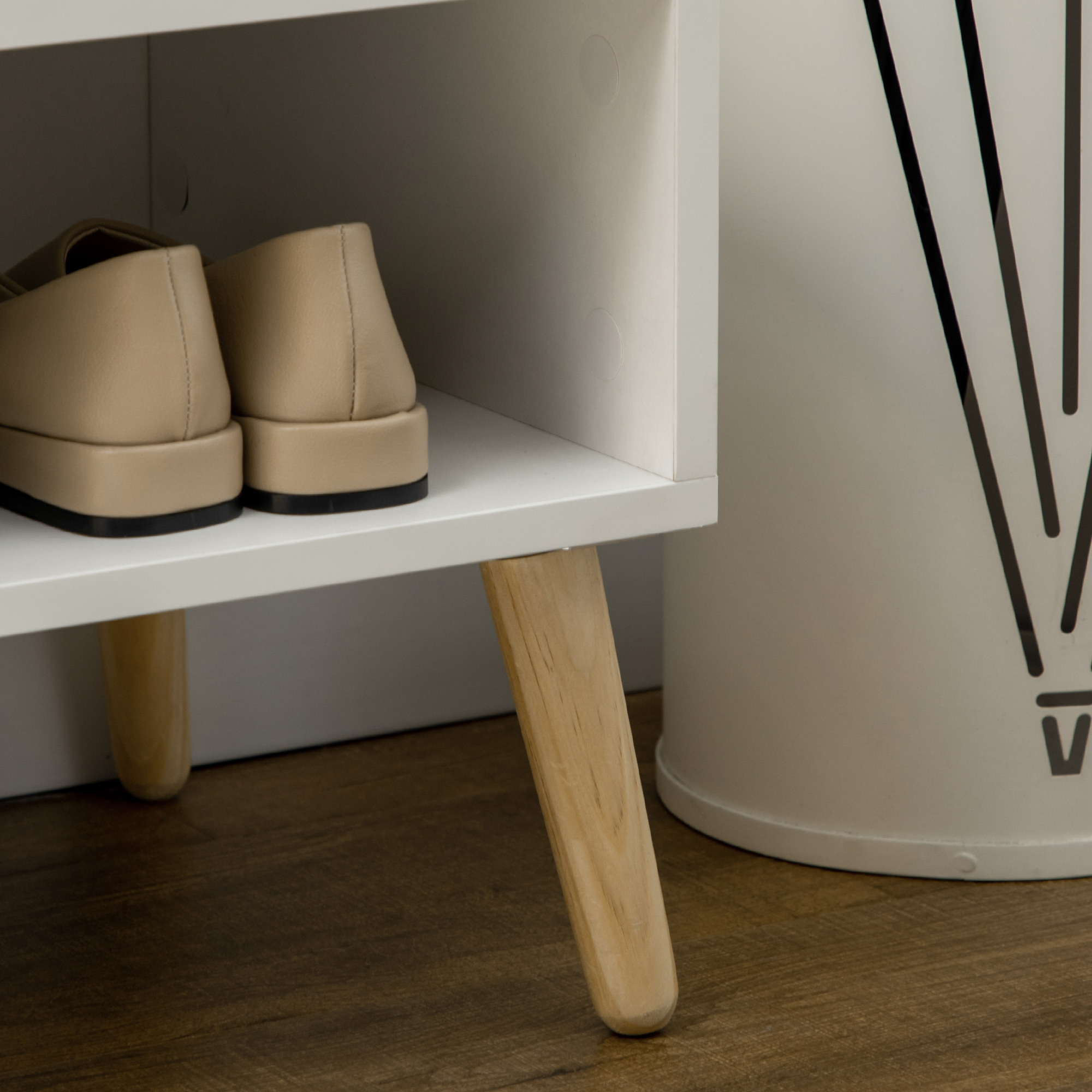 Zapatos planos beige en estante blanco con patas de madera. Un cubo blanco cercano.