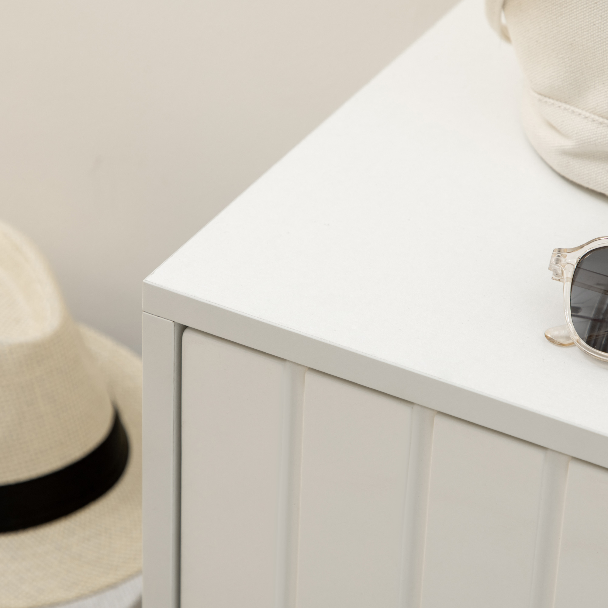 Un sombrero de paja con cinta negra, gafas de sol y bolso sobre mesa blanca.