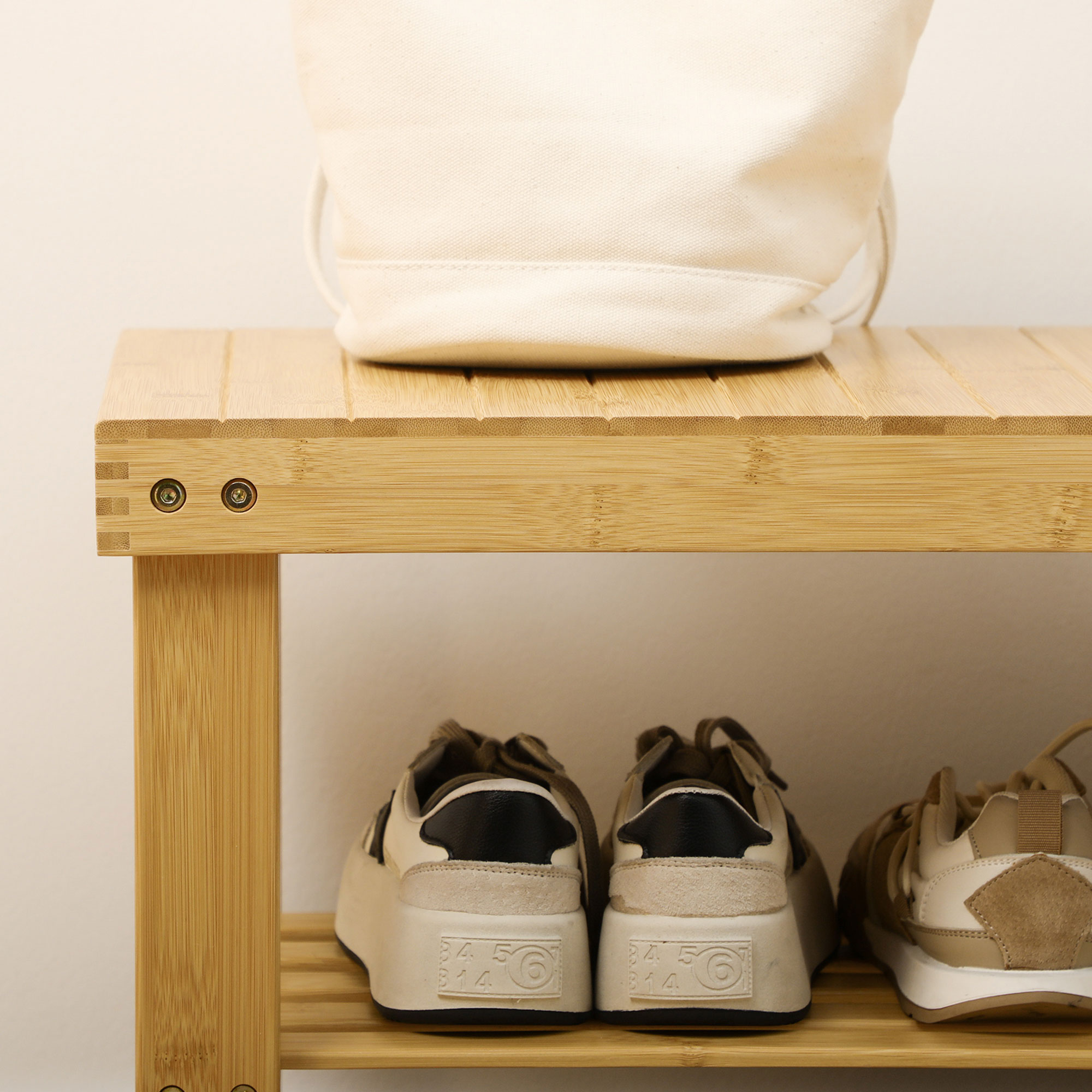 Una bolsa color crema sobre un estante de madera encima de tres pares de zapatillas.