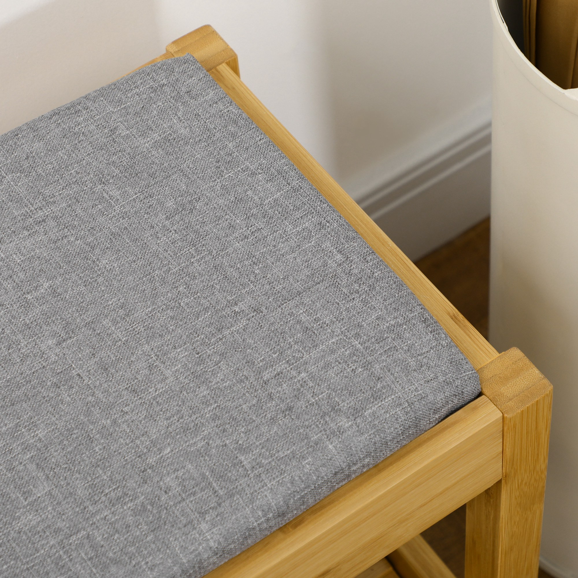 Un taburete de madera con asiento de tela gris junto a un contenedor blanco.