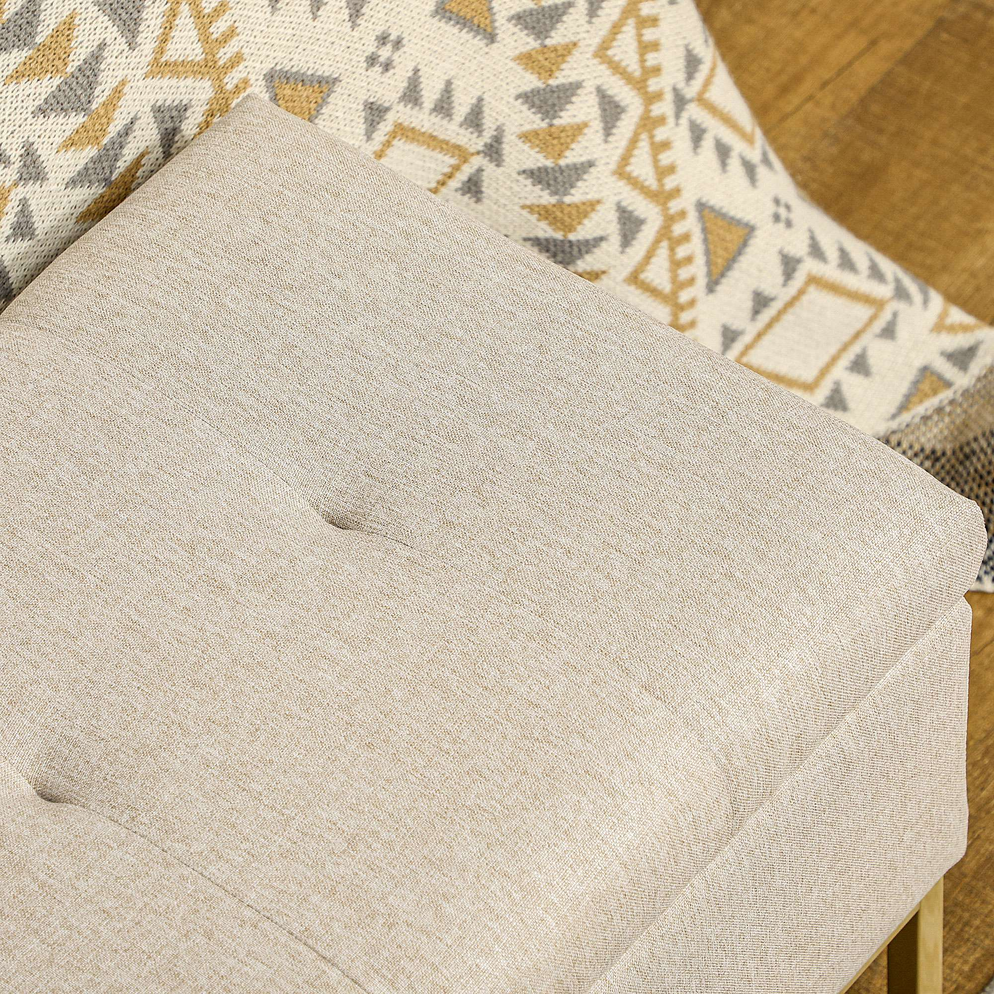 Otomana beige con manta estampada y suelo de madera.