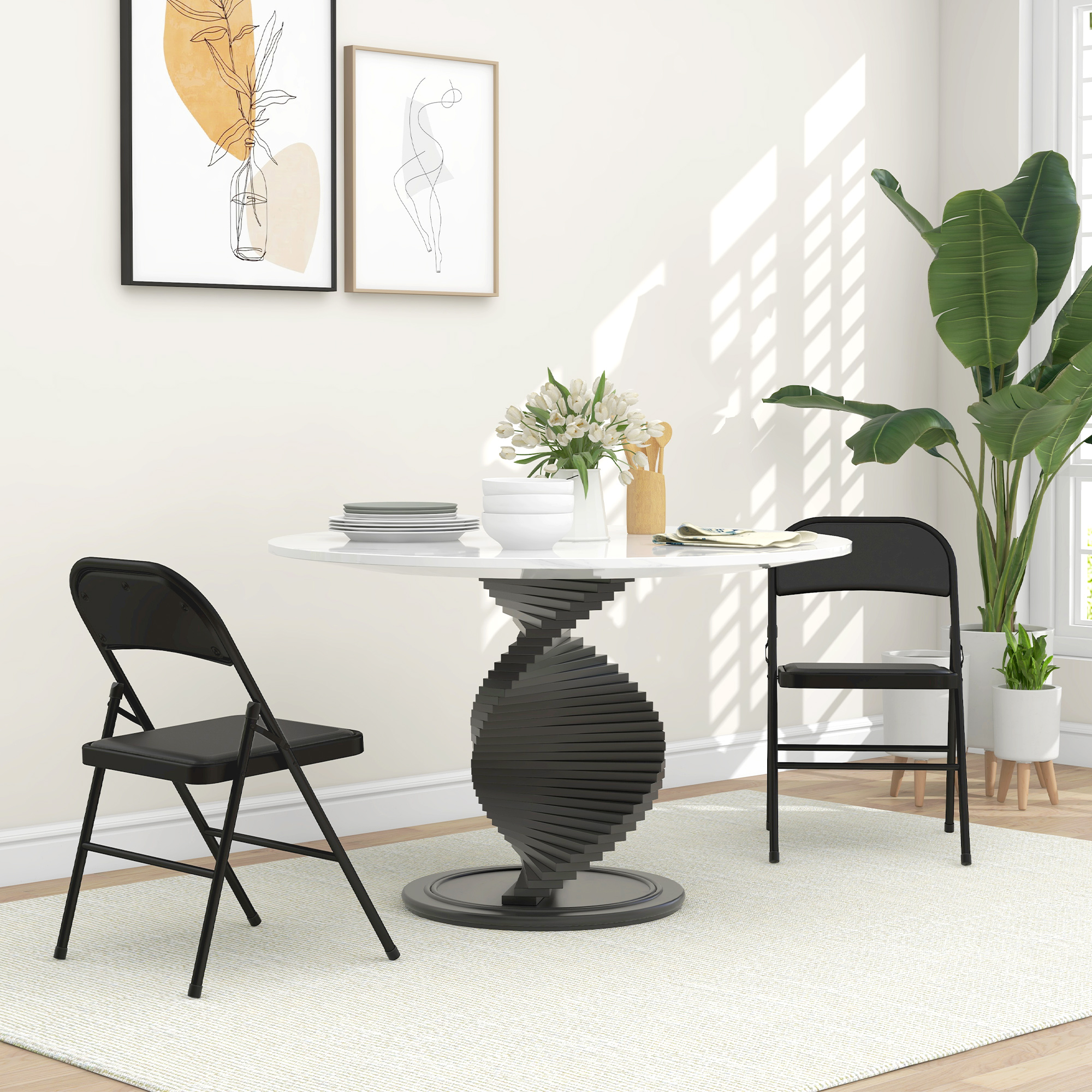 Una mesa redonda blanca con base negra, dos sillas negras, plantas y arte en la pared.