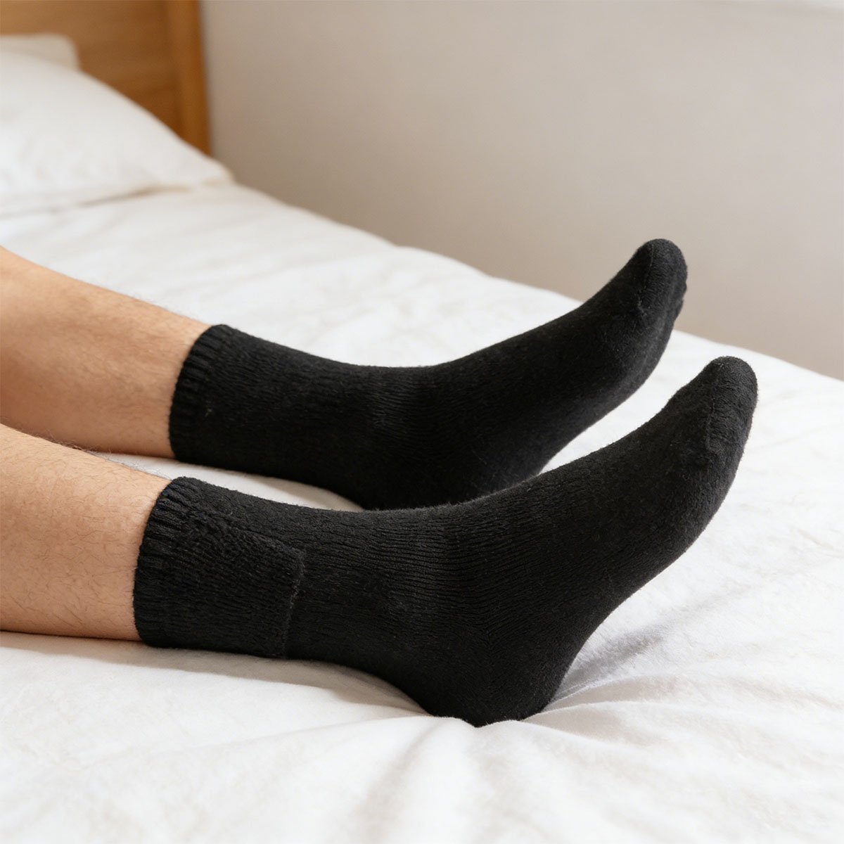 Stopy w czarnych skarpetkach na białym łóżku z drewnianym zagłówkiem.