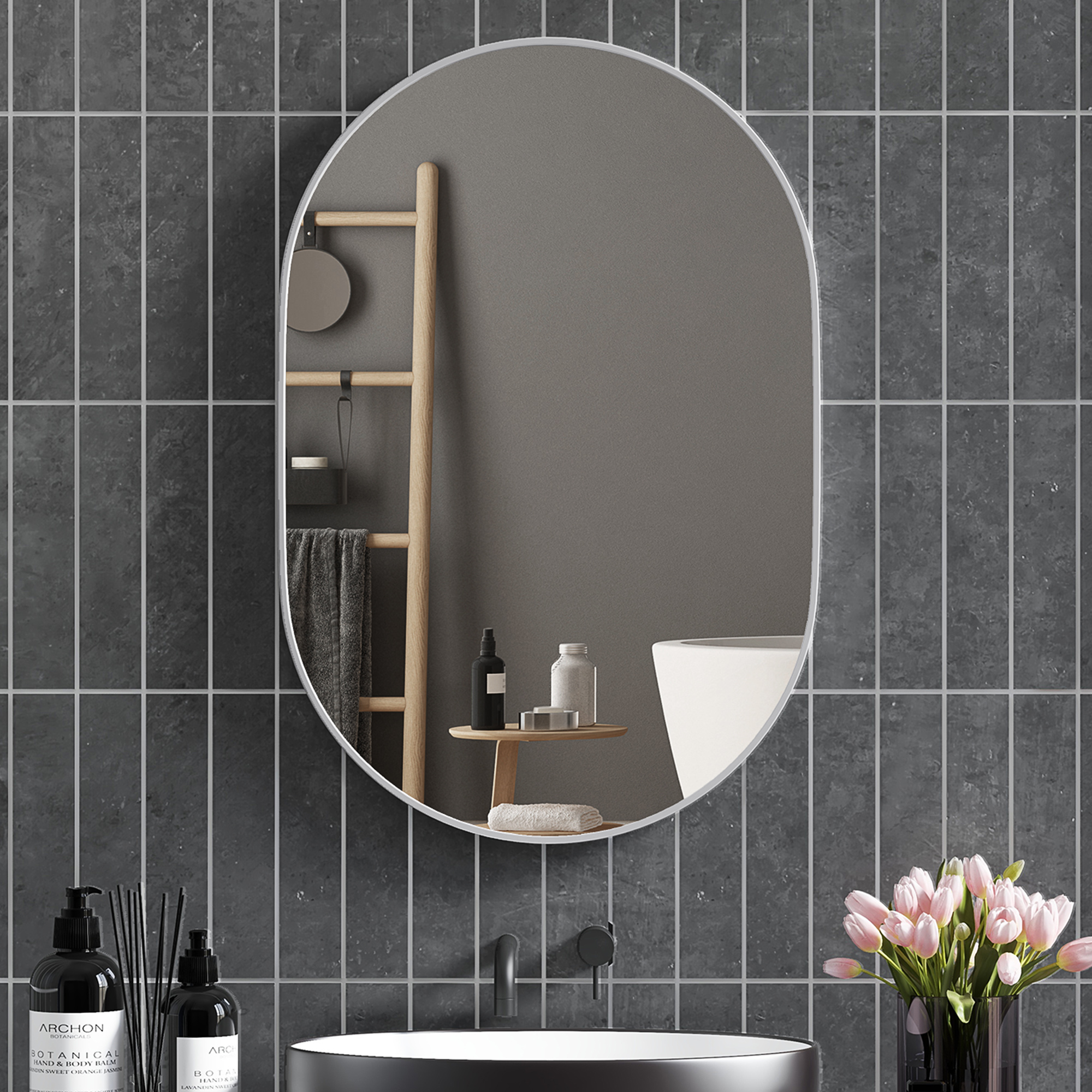 Baño con azulejos oscuros, espejo, escalera, botellas y flores.