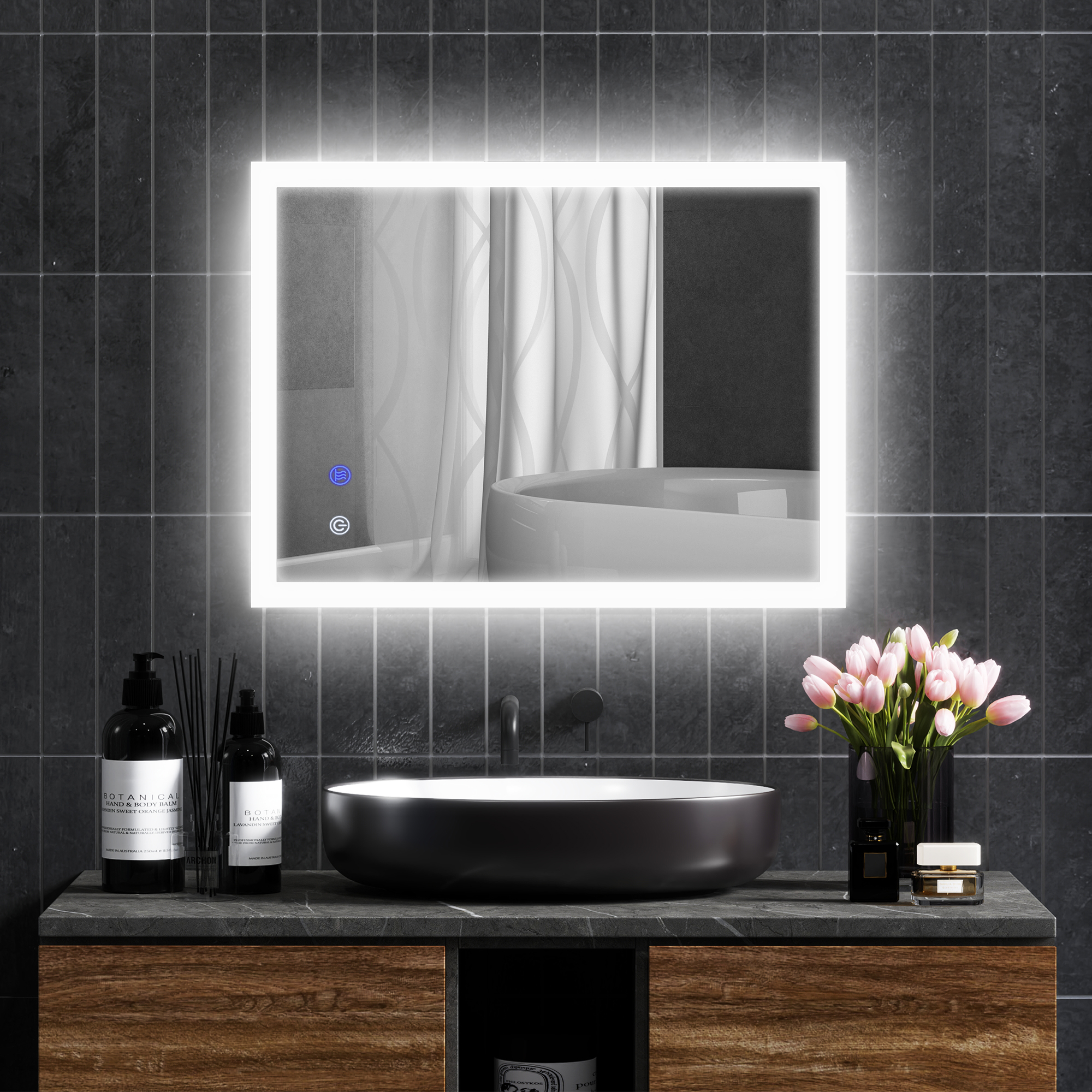 Un espejo retroiluminado sobre un lavabo negro con flores y botellas.