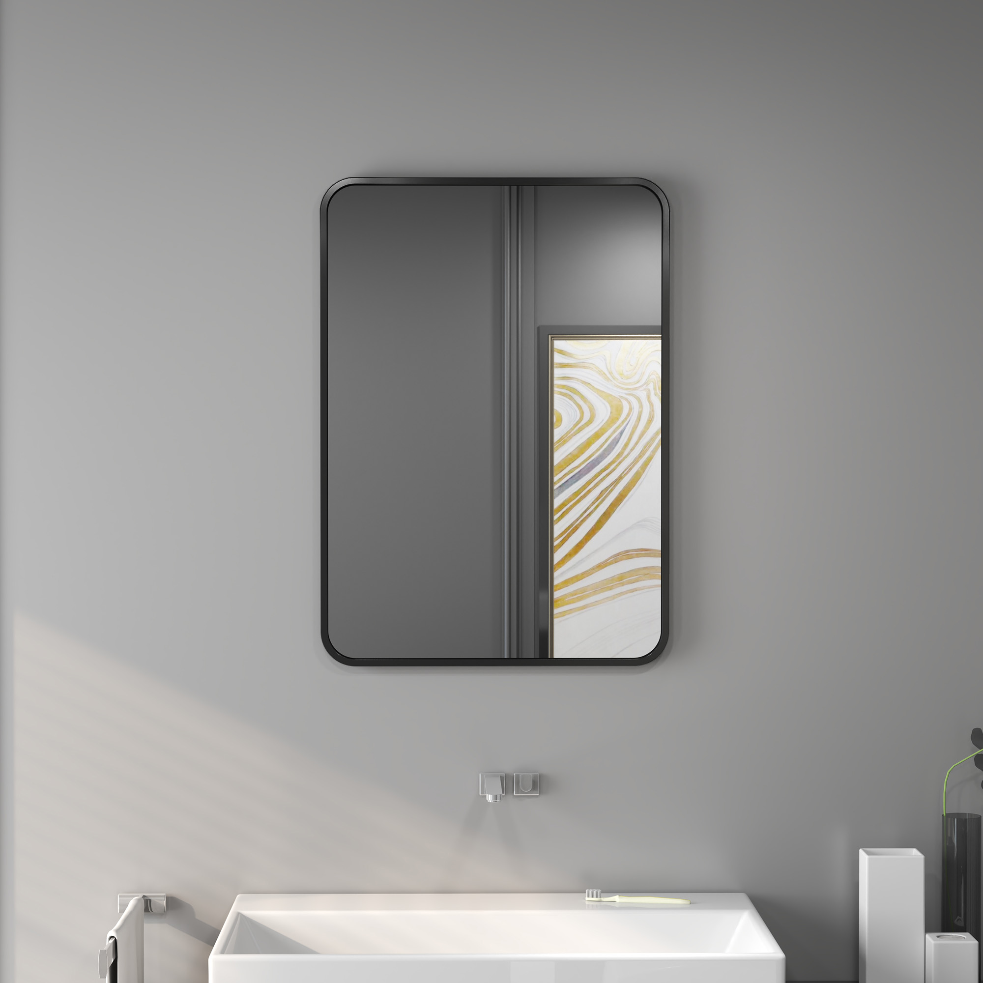 Un espejo rectangular con marco negro cuelga sobre un lavabo blanco. Una imagen está dentro del espejo.