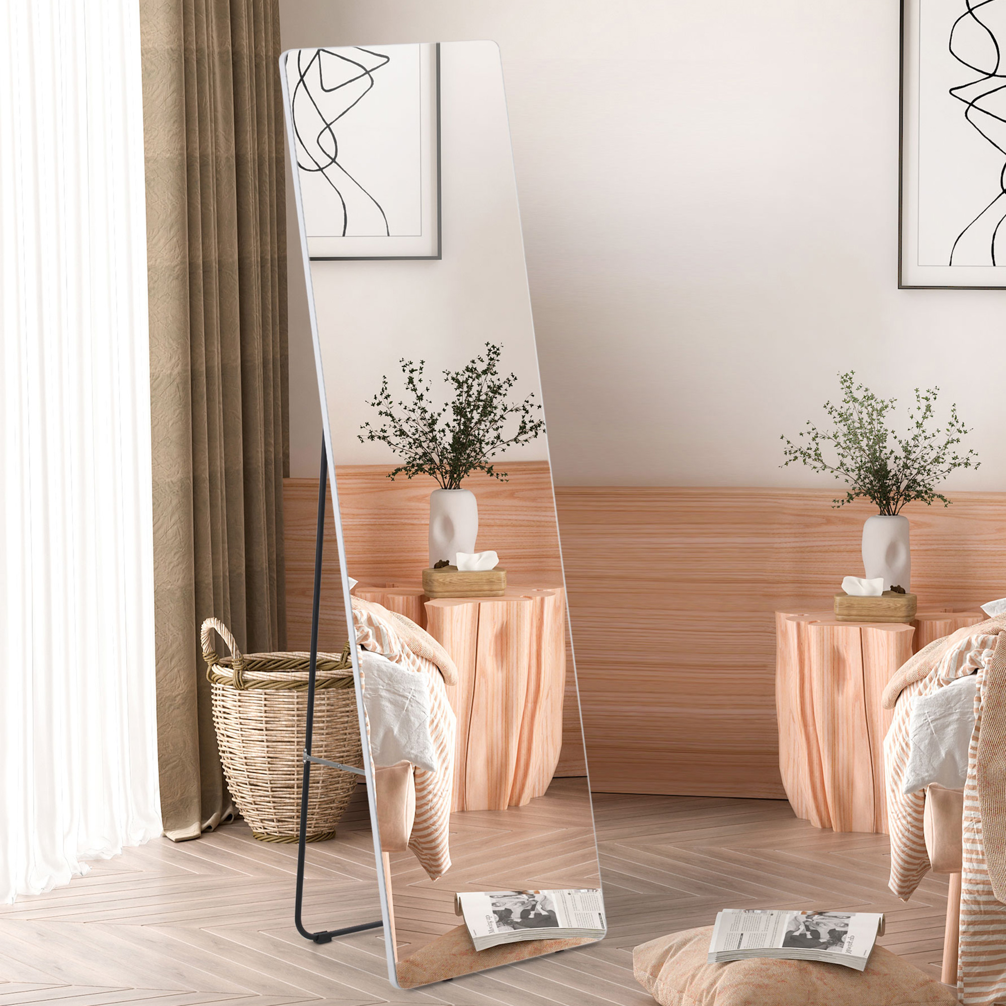 Un espejo alto está en un dormitorio junto a una cesta tejida y cortinas. Arte en la pared.