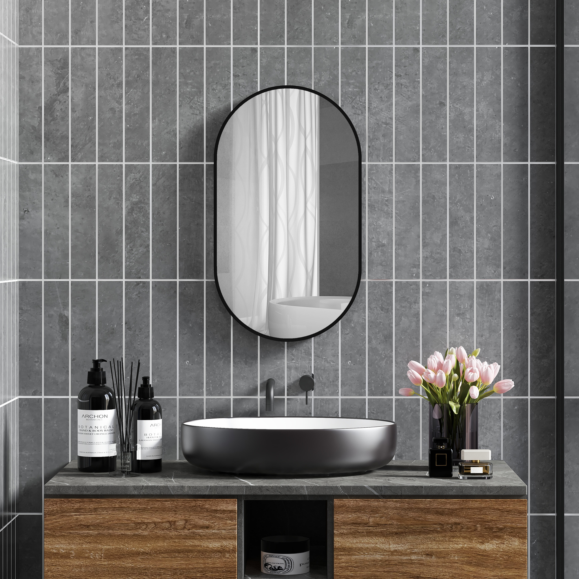 Un tocador de baño moderno con lavabo negro, espejo, flores y botellas.