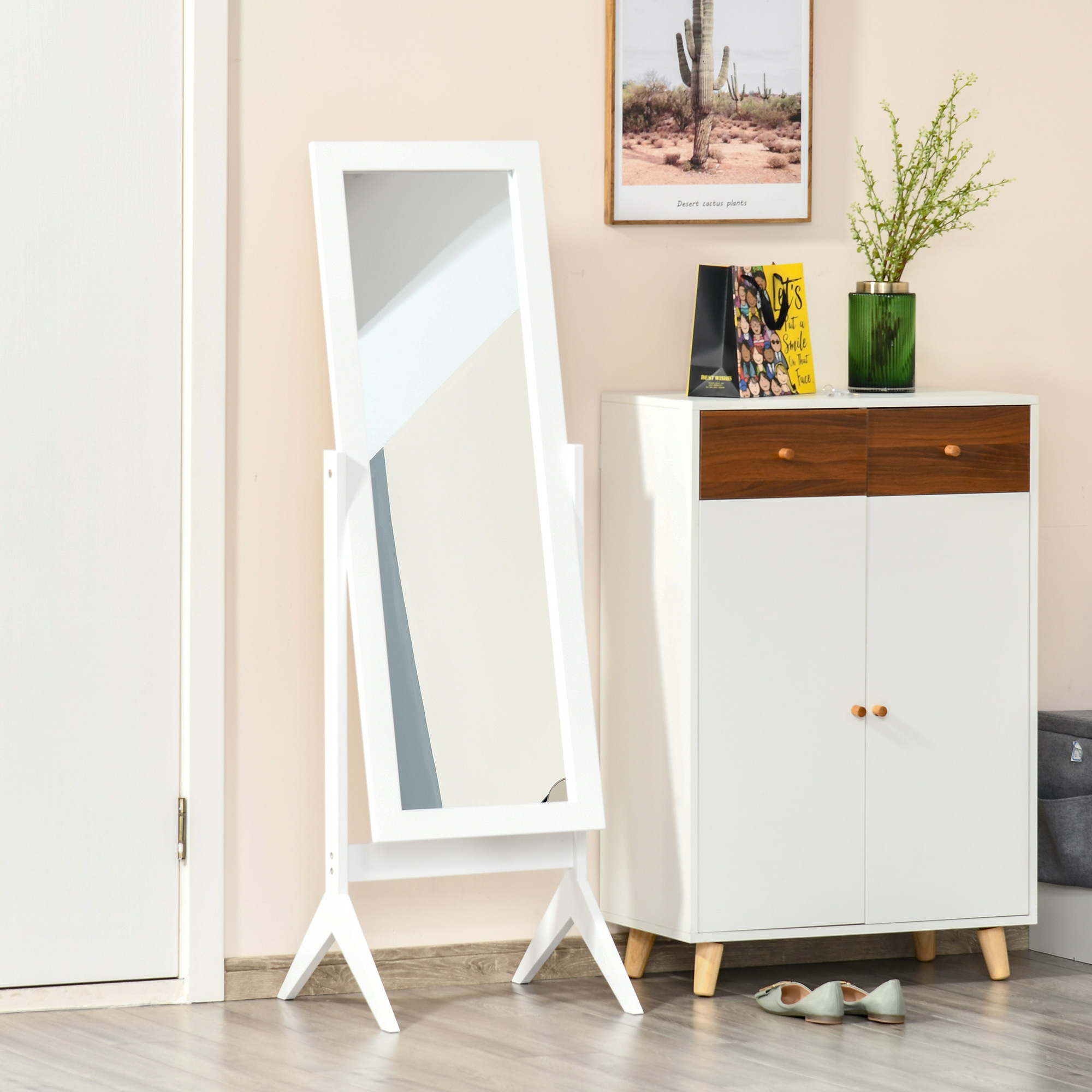 Un espejo de pie blanco junto a un mueble blanco con detalles de madera. Un póster y un jarrón sobre el mueble.