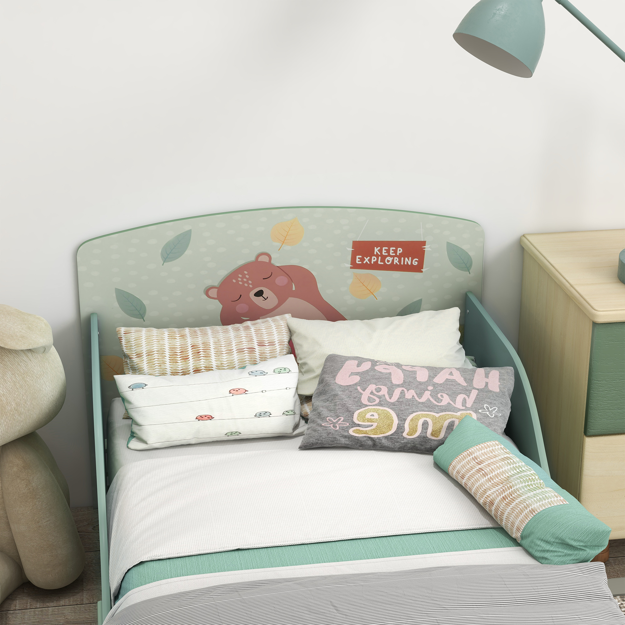 Una cama infantil con motivo de oso, cojines y lámpara.
