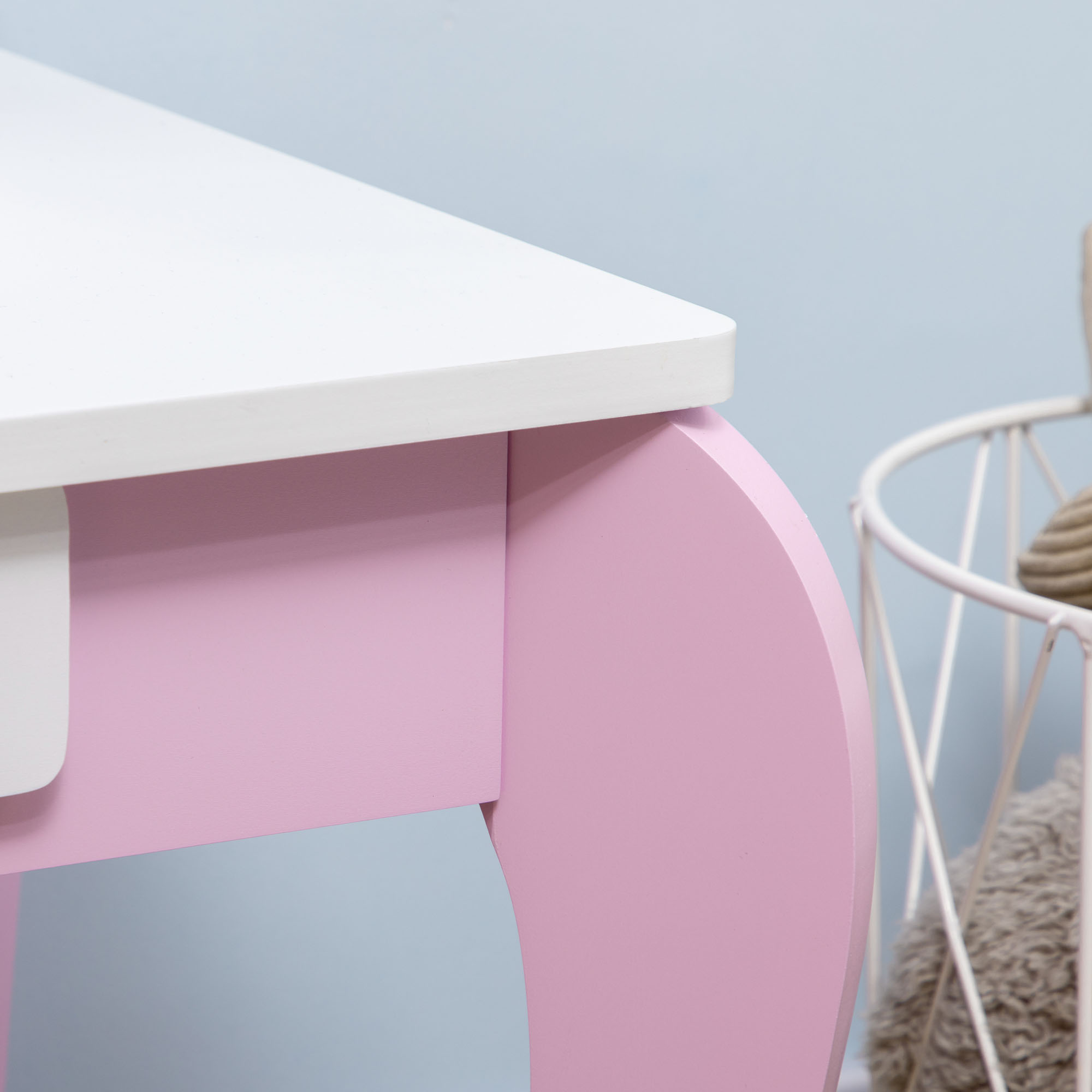 Mesa blanca con detalles rosas ante pared azul claro. Cesta con juguetes a la derecha.