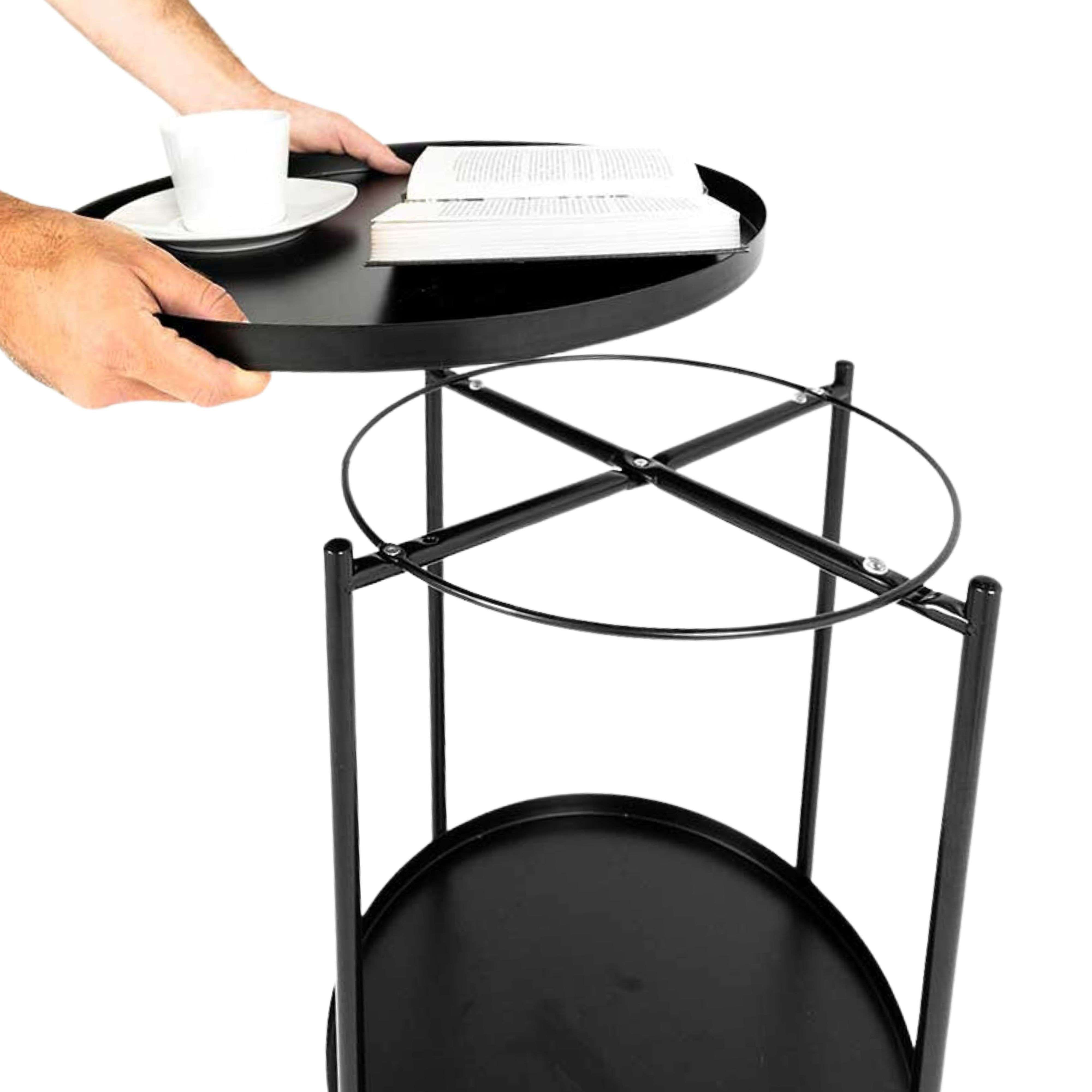 Una mano coloca una bandeja negra con taza y libro sobre una mesa redonda.