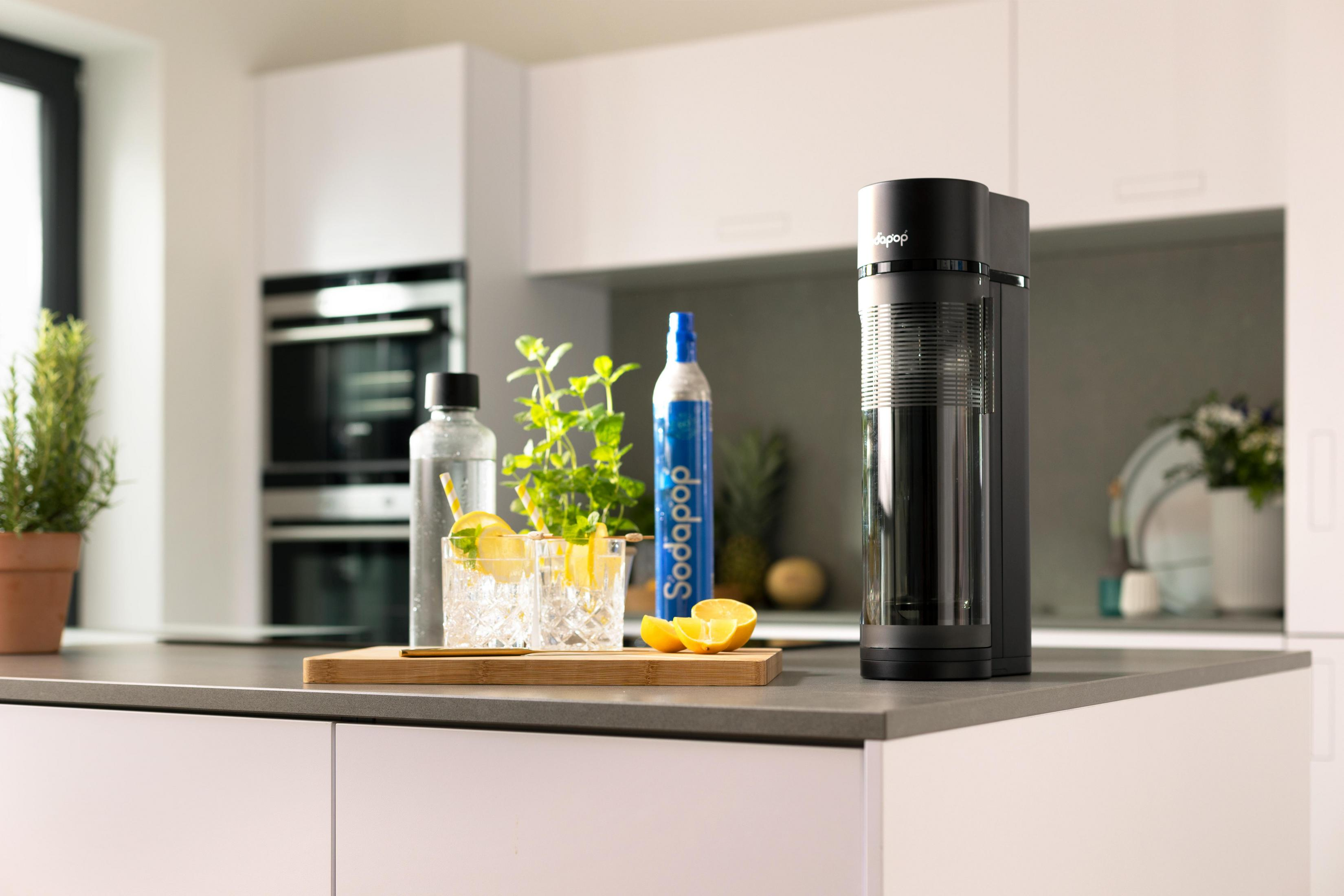 Ein Sodastream-Gerät steht neben zwei Gläsern mit Zitronengetränken und einer CO2-Flasche.