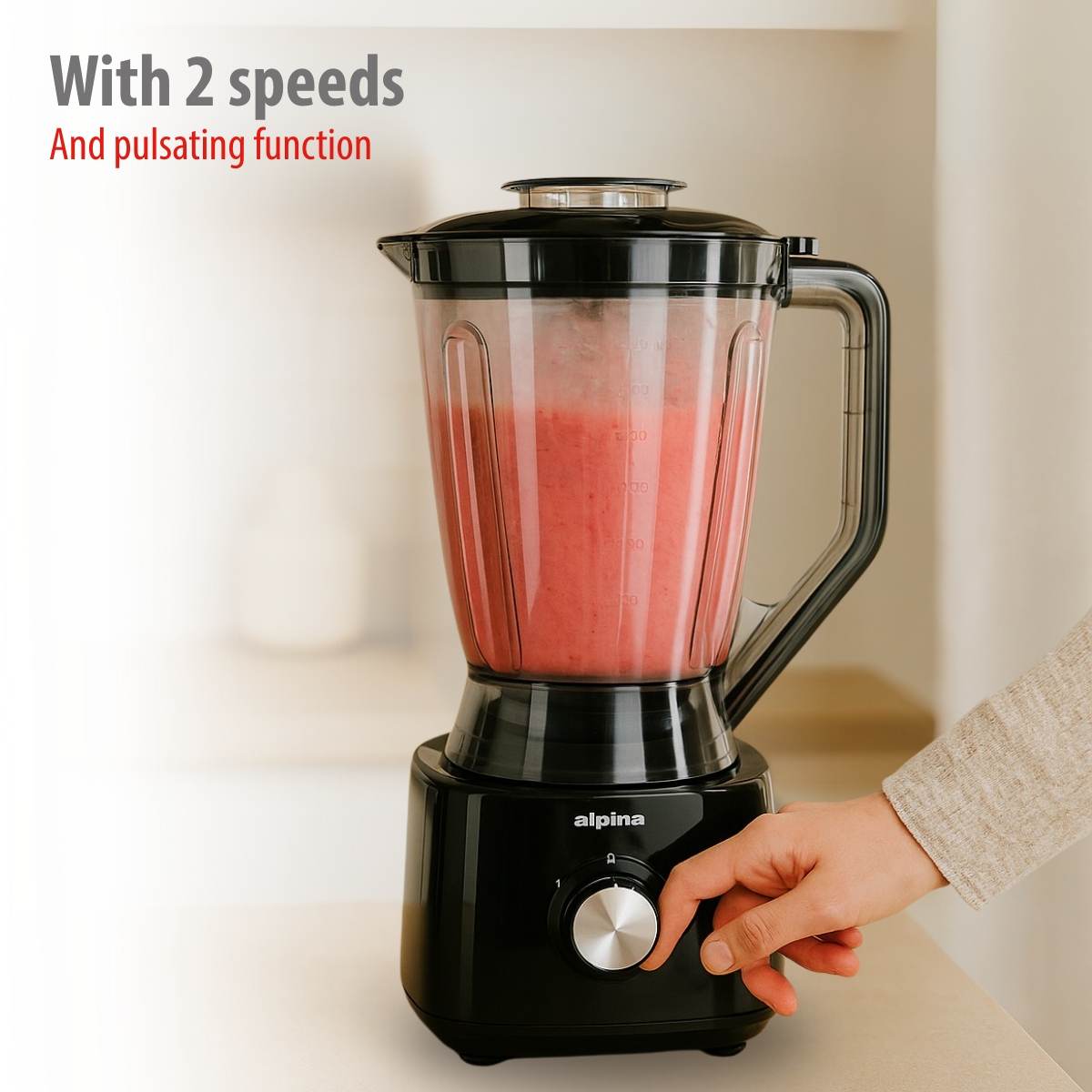 A black blender with a red smoothie and a hand turning the dial.