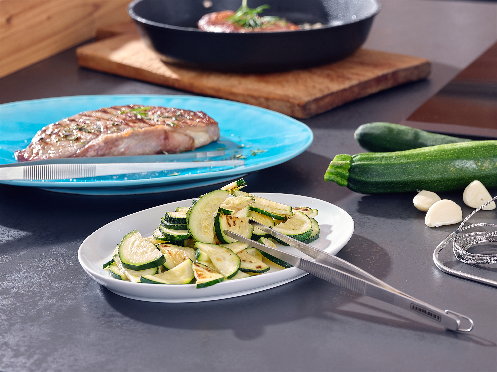 Bistecca alla griglia su piatto blu con zucchine affettate, aglio e zucchine intere.