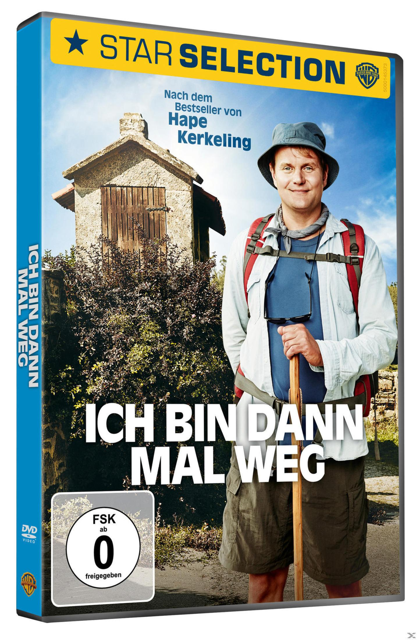 Ein Mann mit Hut und Rucksack steht vor einem Steinhaus und Büschen.