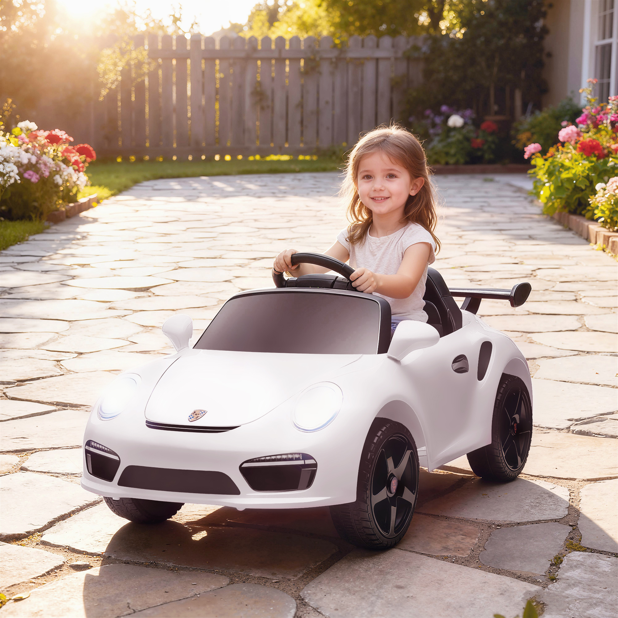 Una niña sonriente conduce un coche de juguete blanco por un camino de piedra en un patio soleado.