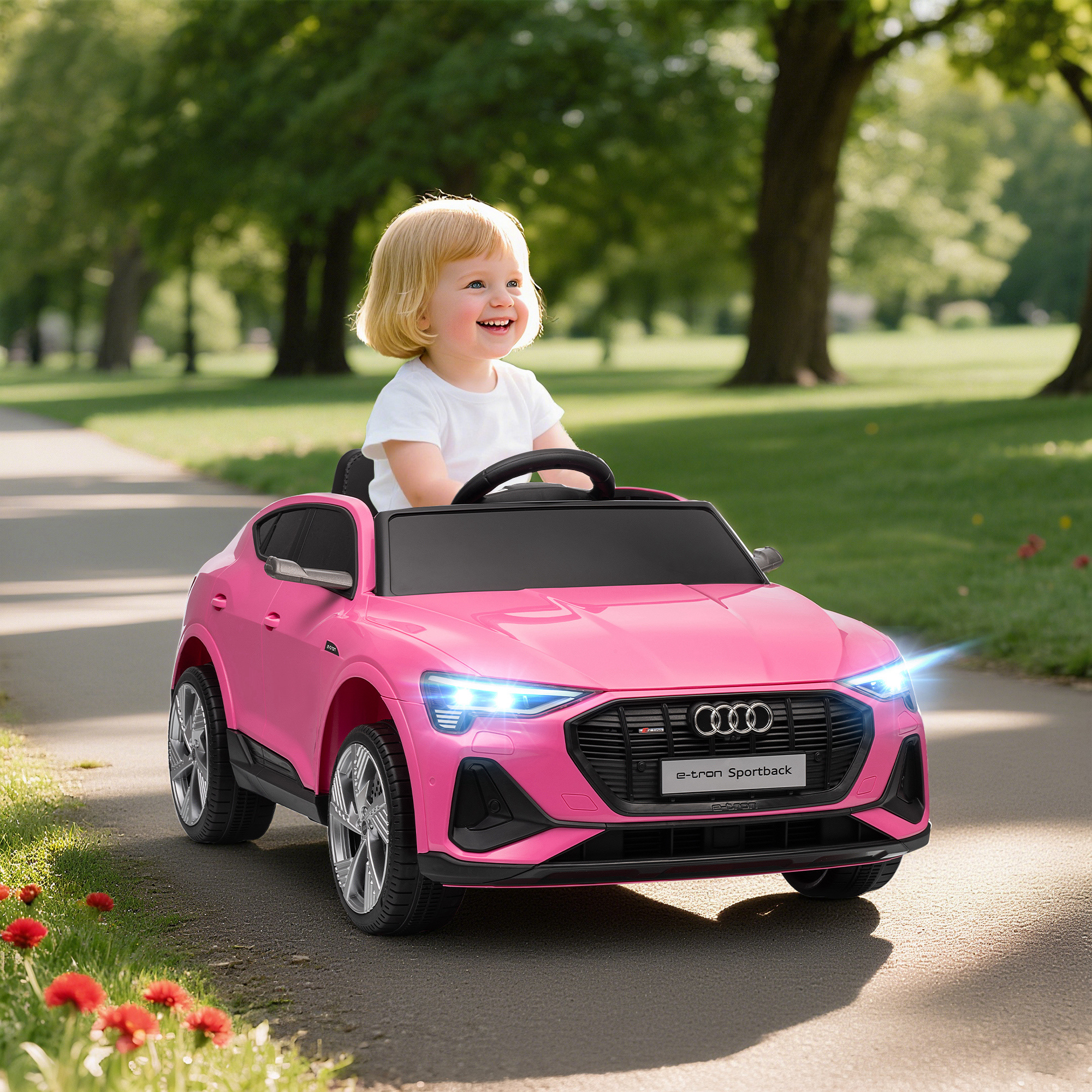 Una niña pequeña conduce un coche de juguete Audi rosa en un camino del parque.