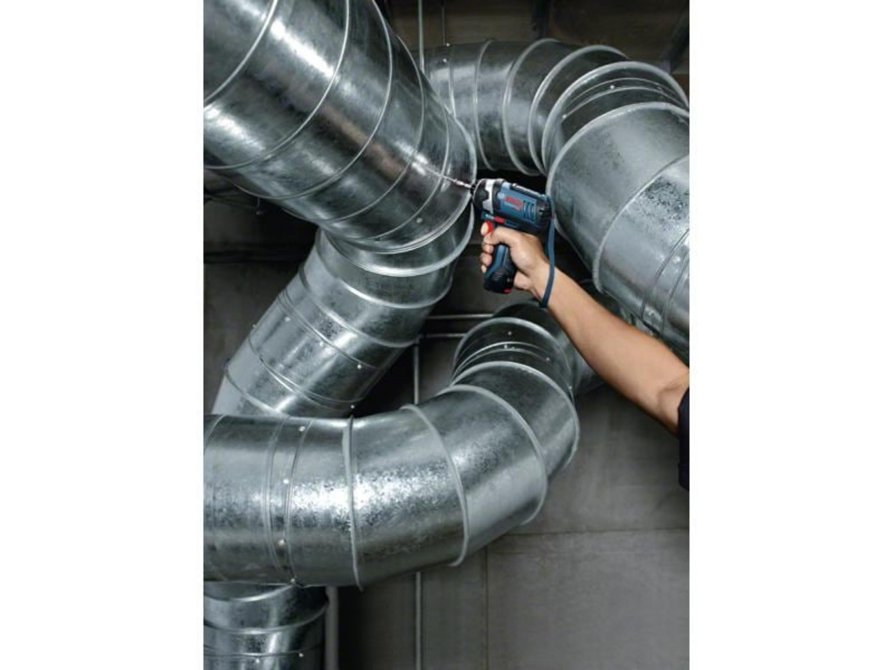 Ręka wierci w metalowym kanale. Niebieska wiertarka w prawej ręce.