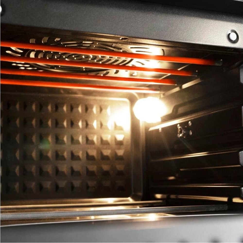 Oświetlone wnętrze piekarnika z czerwonymi elementami grzewczymi i wentylatorem.