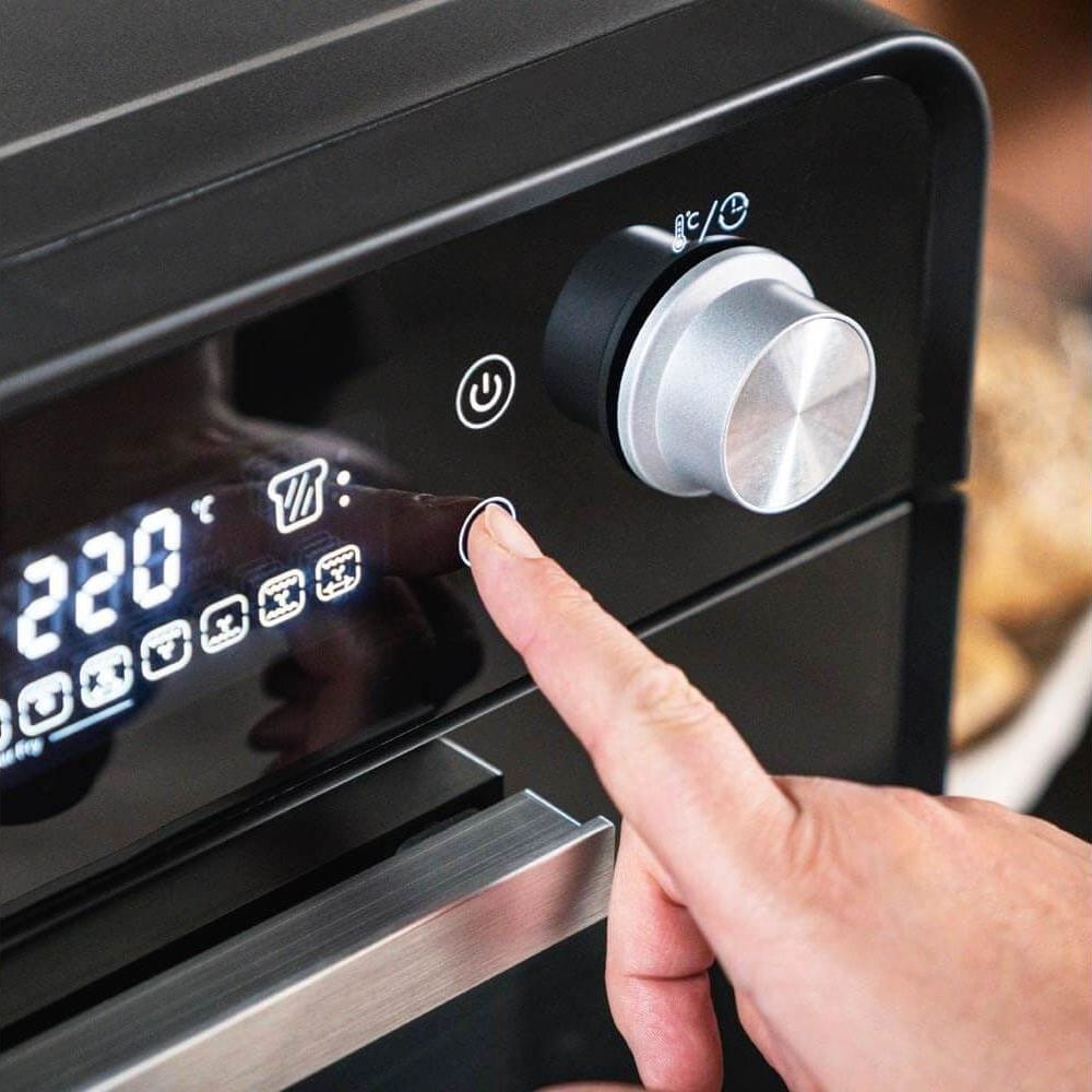 Palec naciska przycisk na cyfrowym wyświetlaczu czarnego piekarnika.