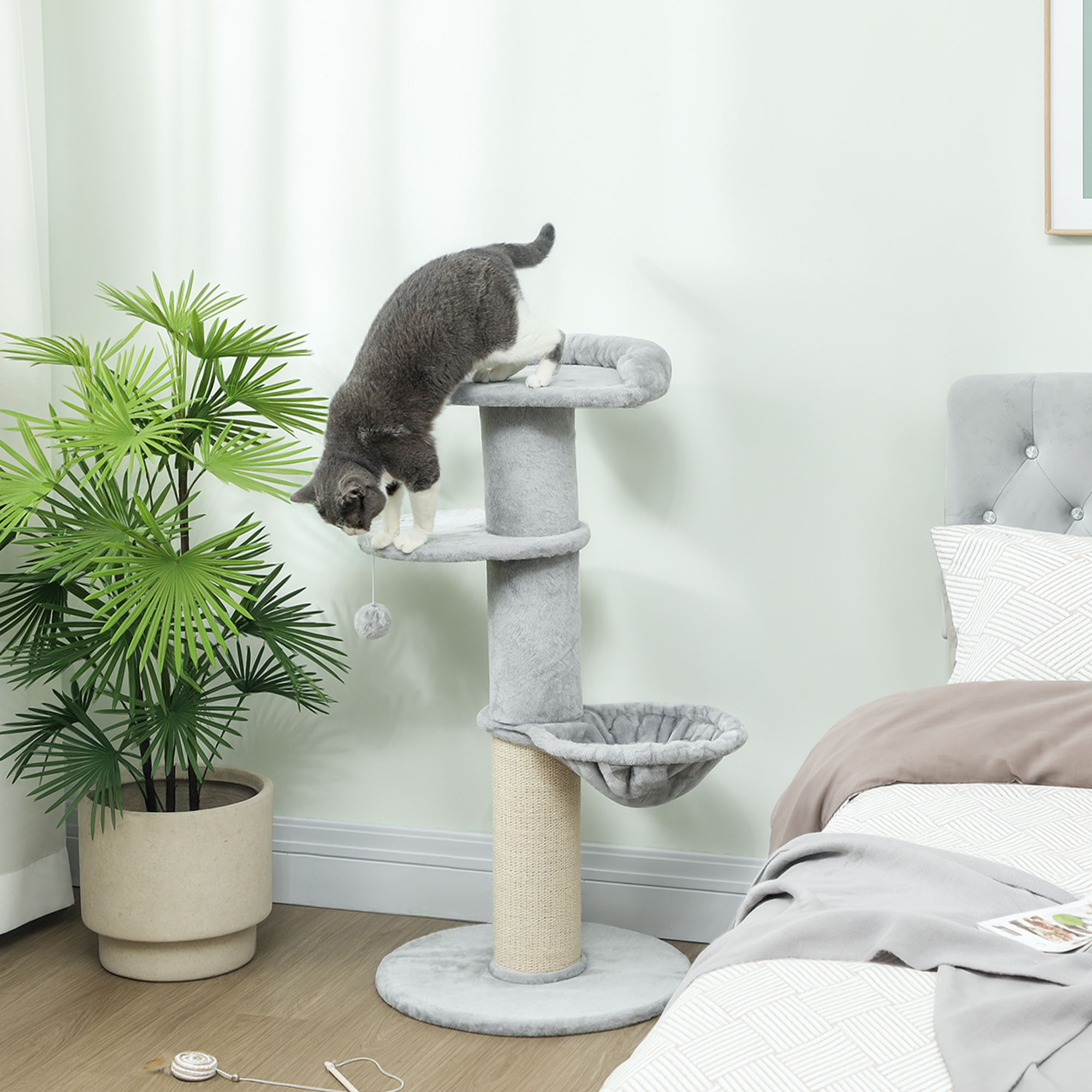 Un gatto si arrampica su un tiragraffi grigio in una camera da letto con piante.